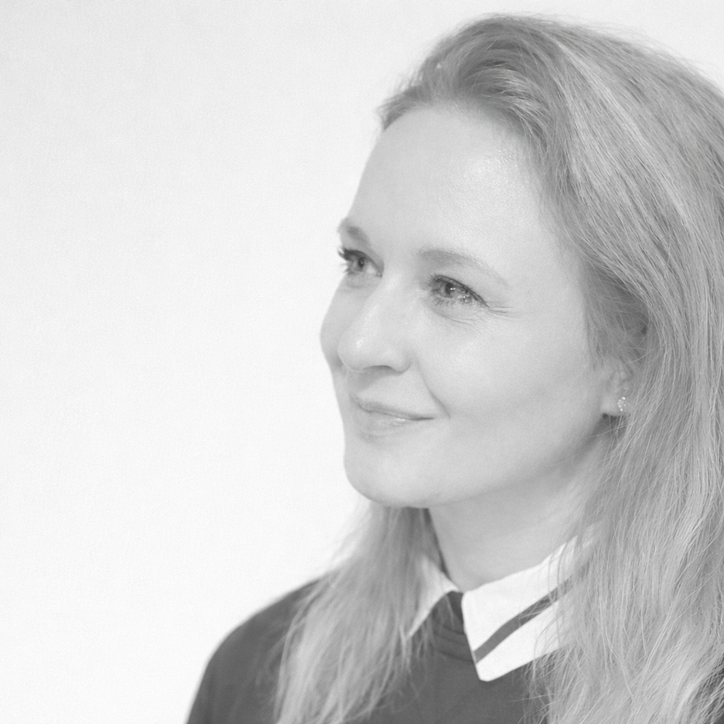 Nahaufnahme eines lächelnden Frauenkopfs in Schwarz-Weiß, mit langem Haar, die nach rechts schaut.