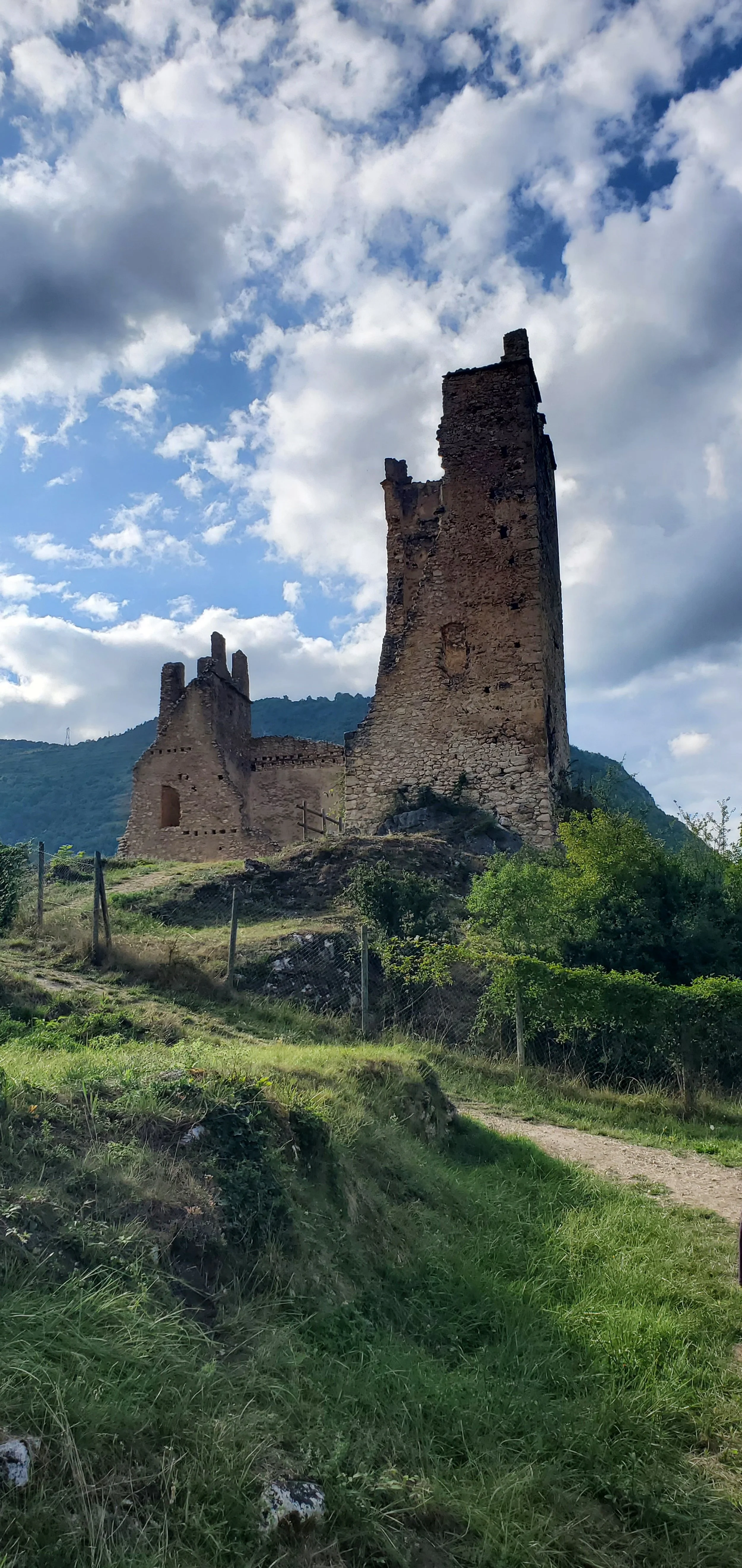 Ruins of an ancient stone castle on a grassy hill with a cloudy sky and mountains in the background.