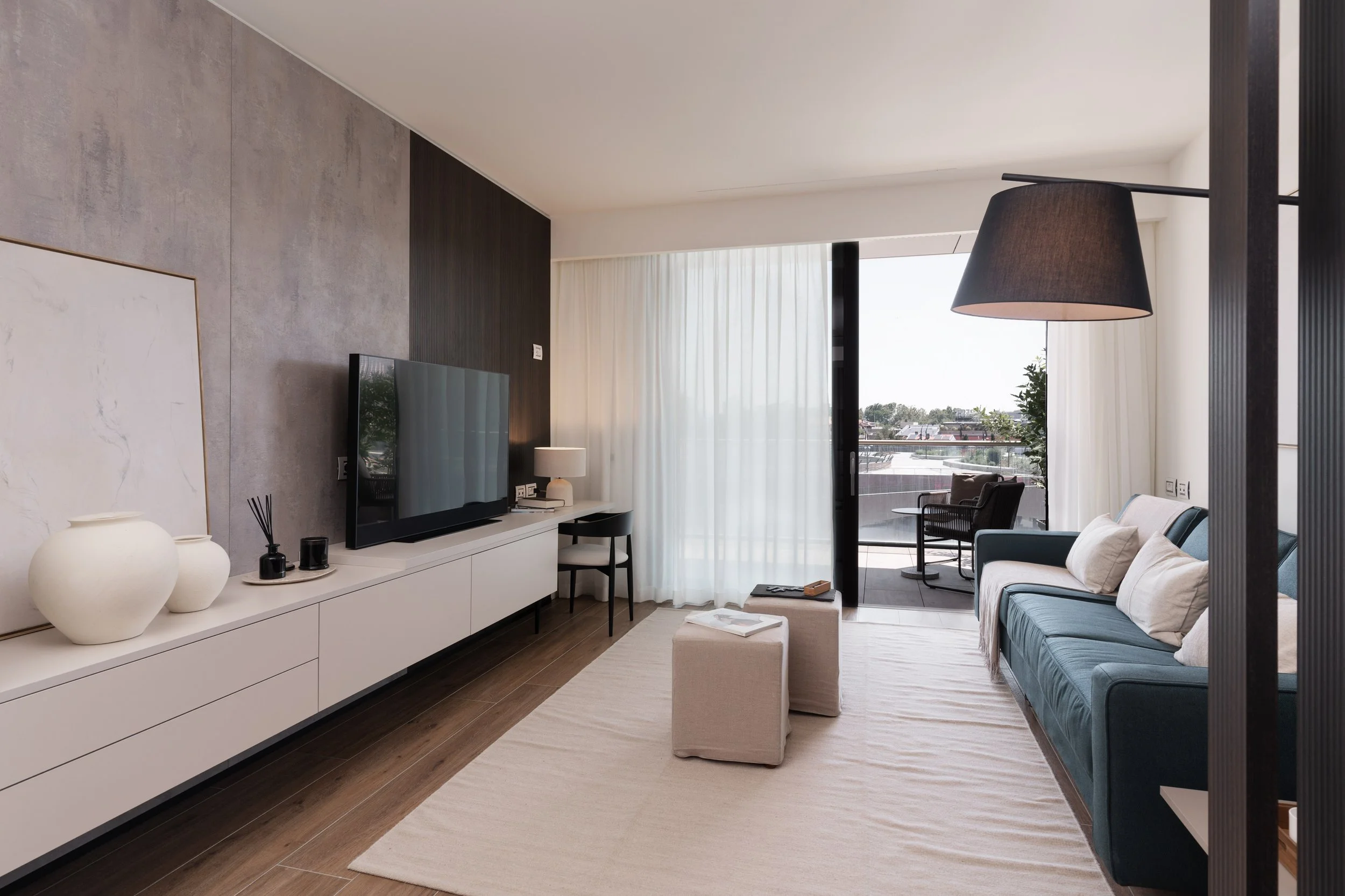 Soggiorno moderno con divano blu, tv, scrivania, lampada da tavolo e area esterna con sedie e vista panoramica