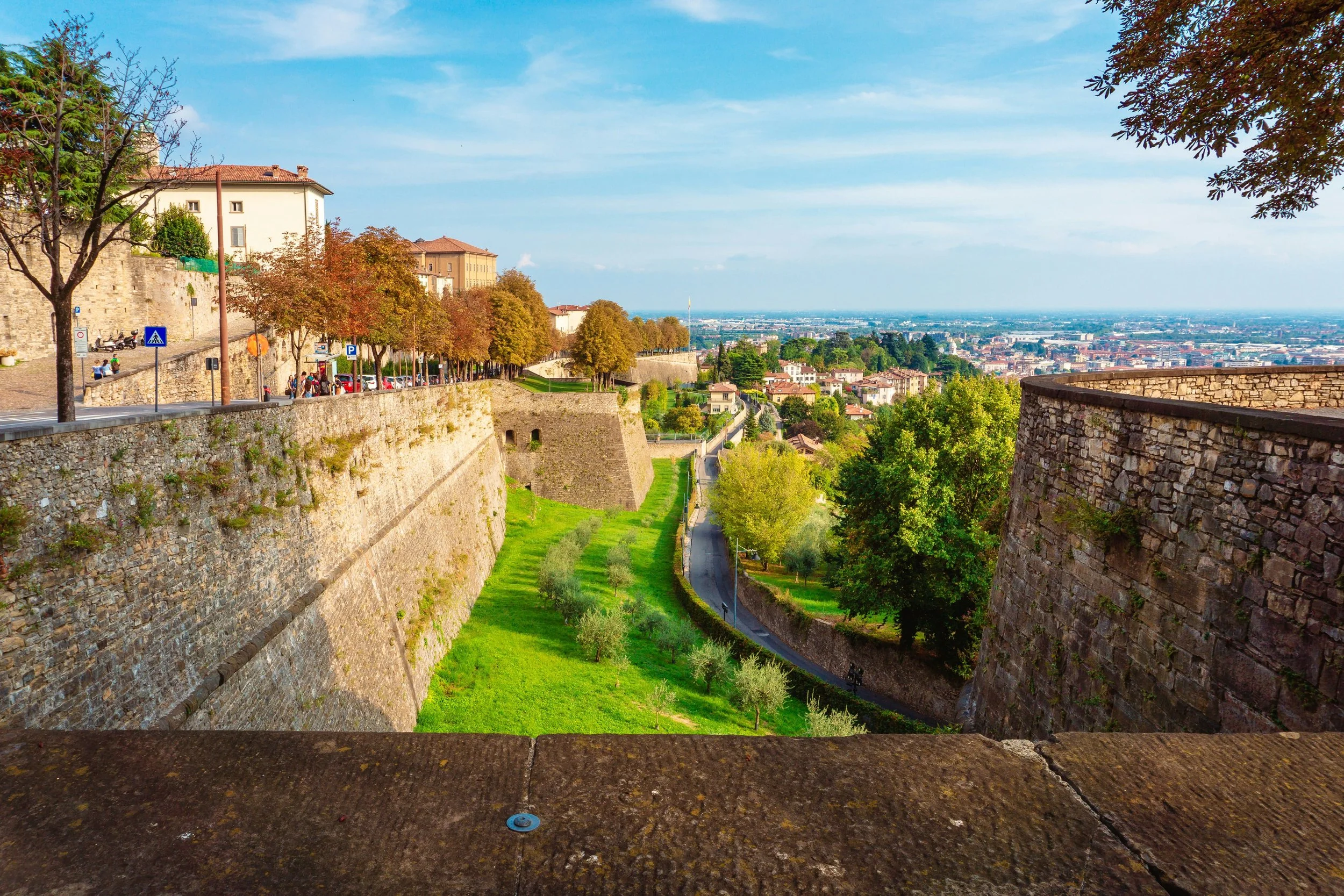 Veduta di una città con mura antiche, alberi e strade, vista verso un paesaggio urbano e campagna.