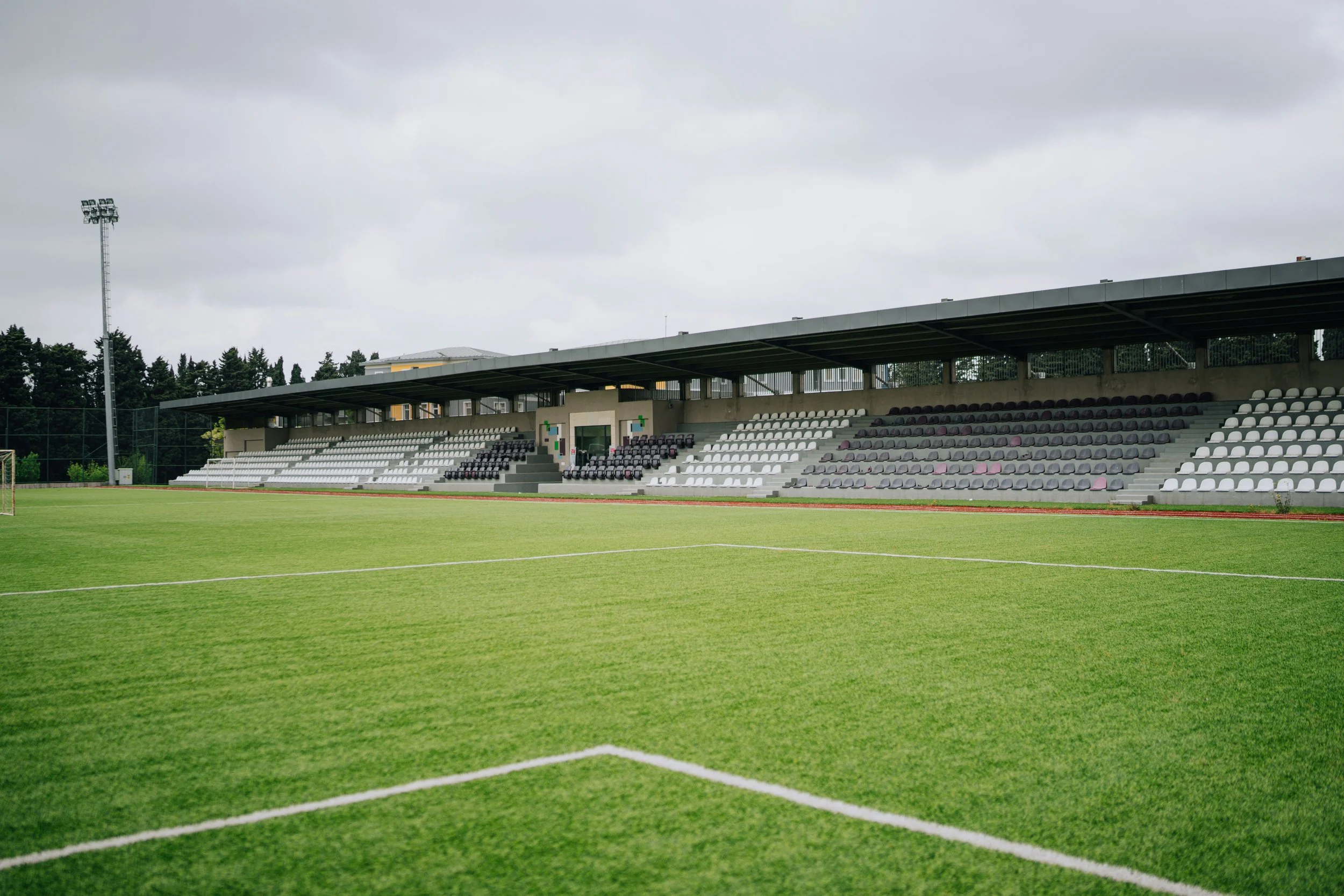 Stadio di calcio con tribune vuote e campo in erba verde, sotto cielo nuvoloso.