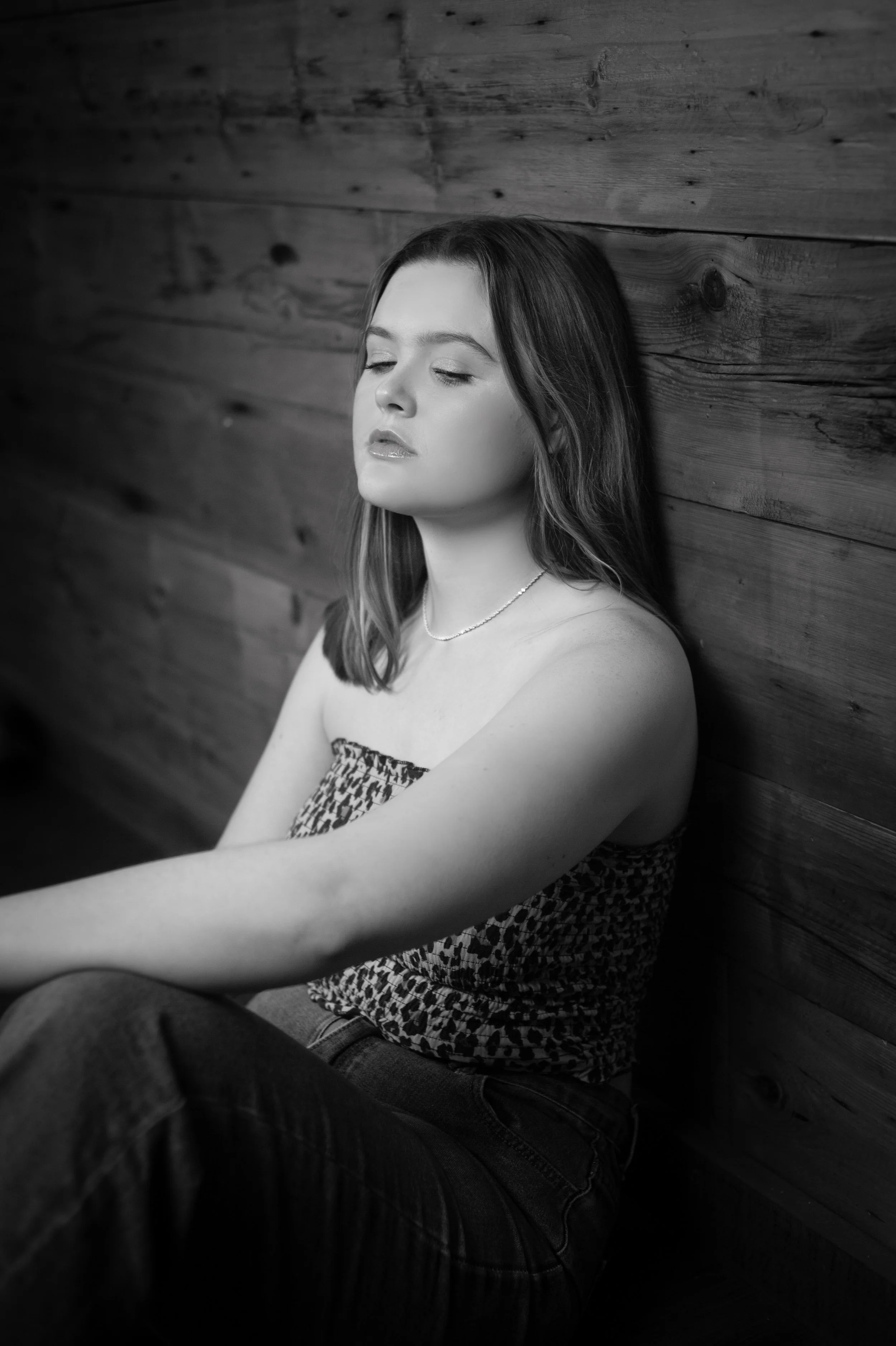 Abi Mack sitting against a wooden wall with her eyes closed. image is in black and white.