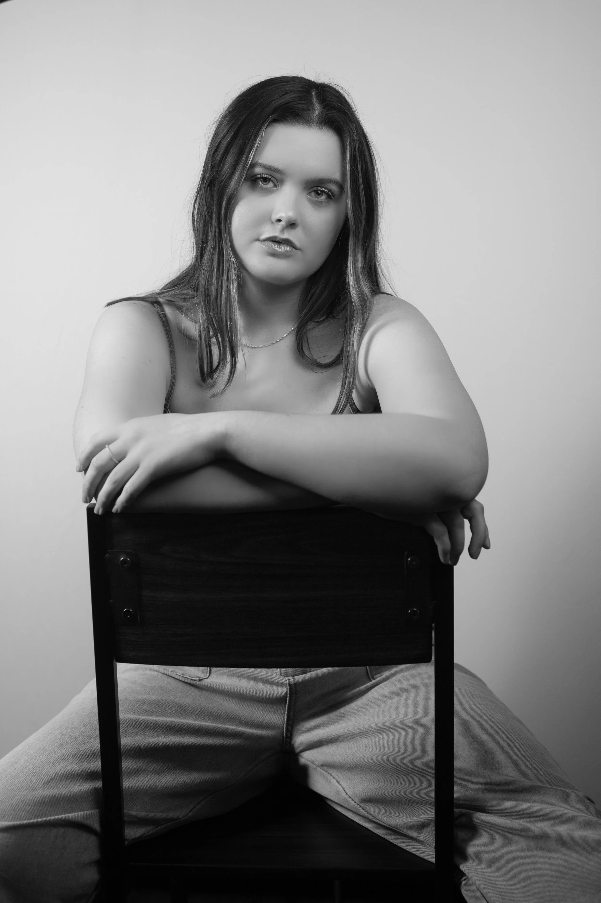 Abi Mack sitting crossed armed backwards on a stool, image is in black and white.