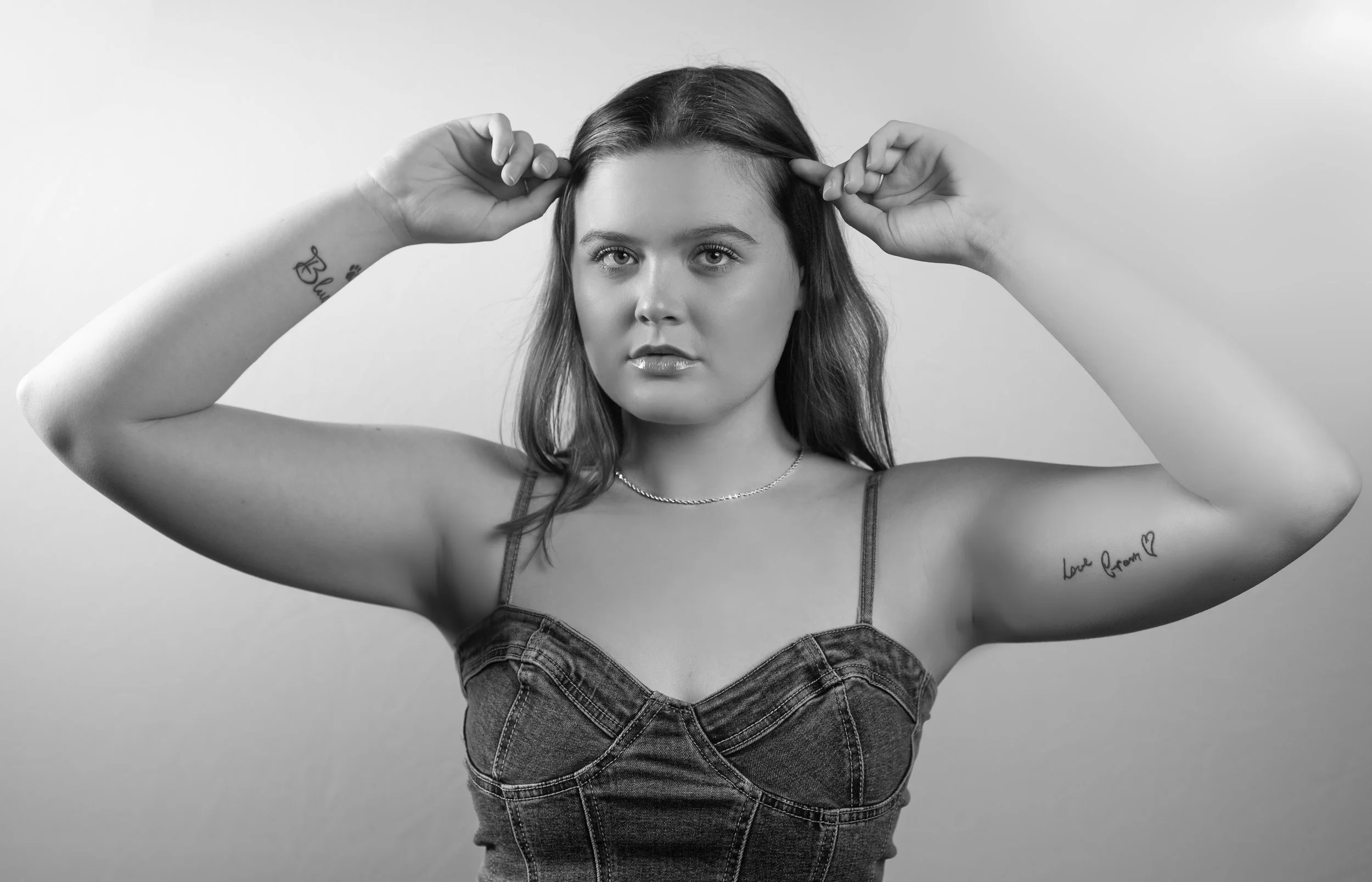 Abi Mack with both her hands to the side of her face pushing her hair back, image is in black and white.