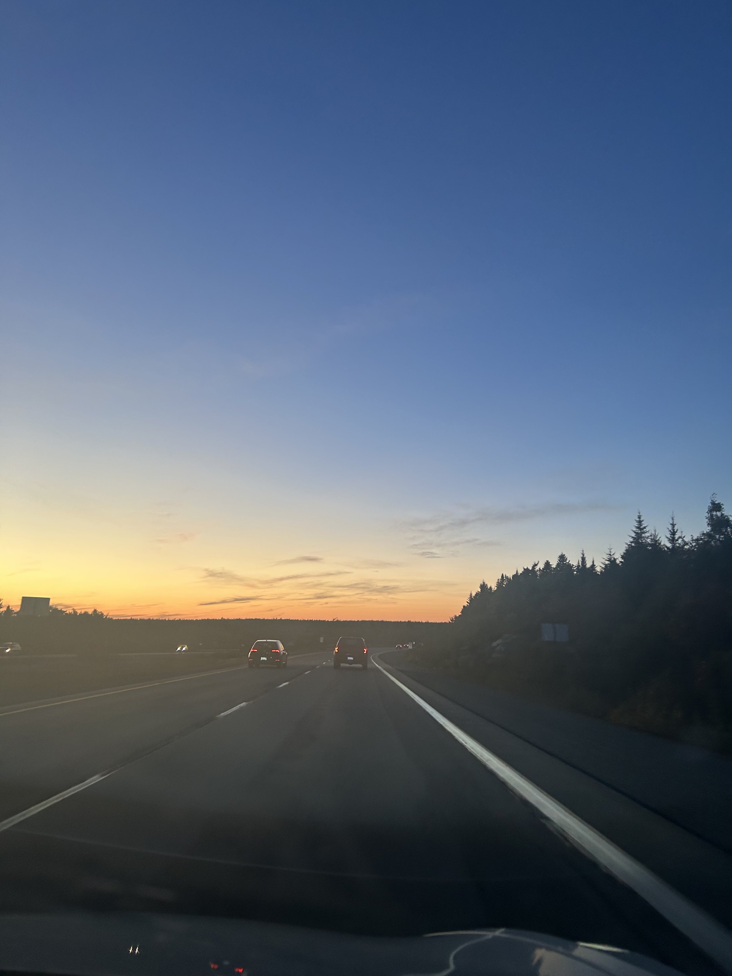 A highway scene at sunset with a clear blue sky, trees on the right side, and several cars driving on the road.