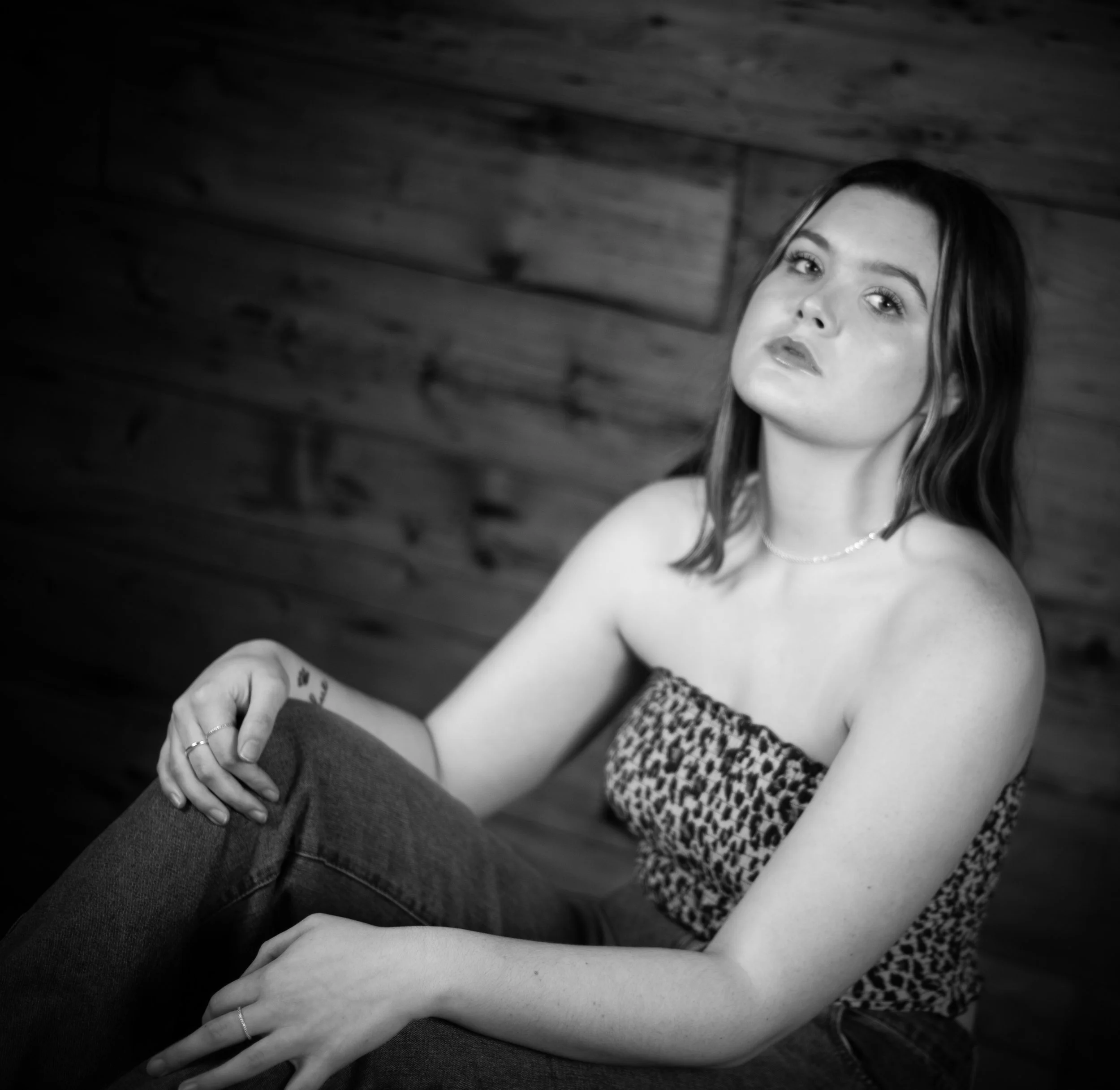 Abi Mack with her head tilted towards the ceiling, sitting, leaning against a wall, image is in black and white.