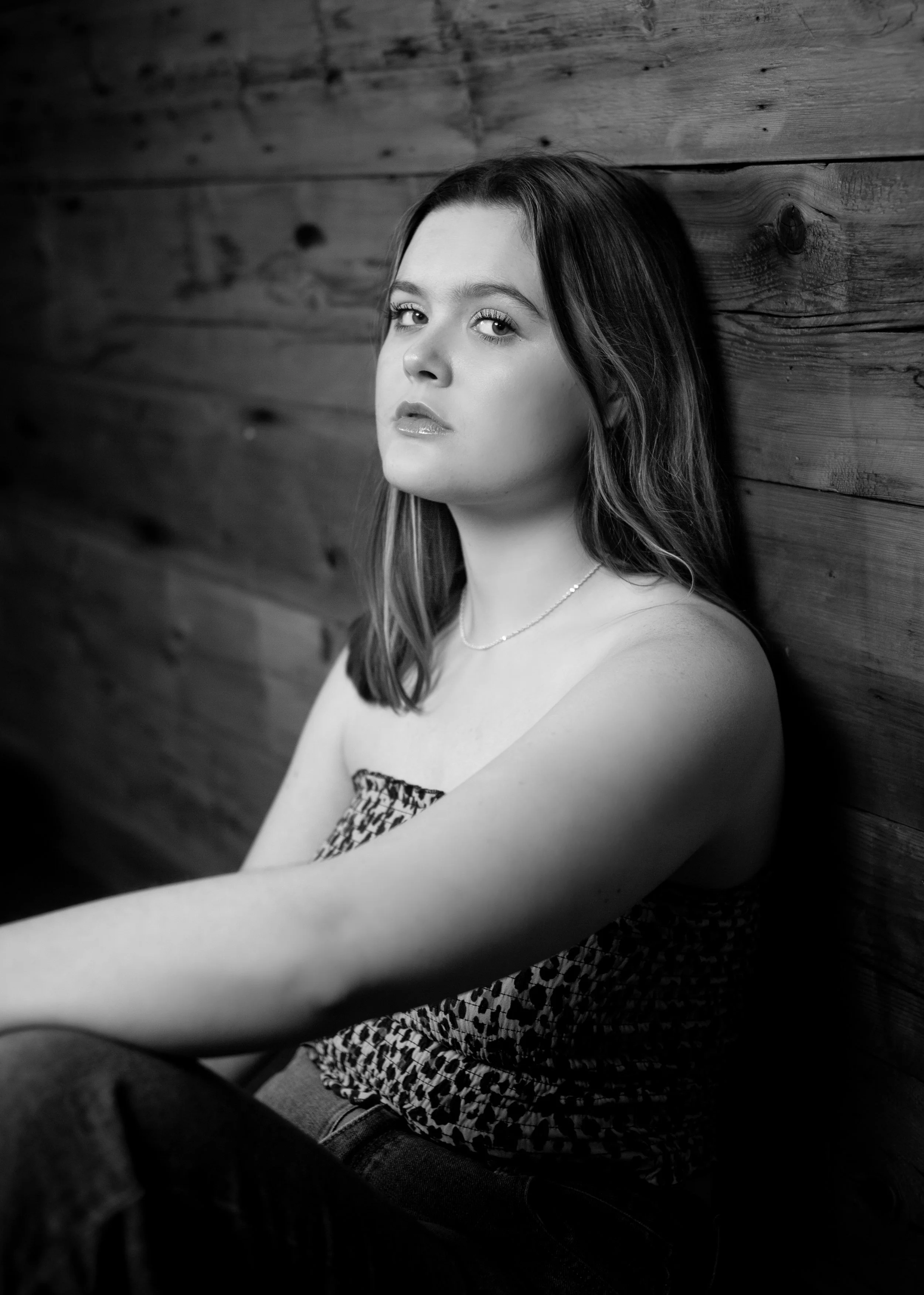 Abi Mack looking at the camera with her back against a wooden wall, image is in black and white.