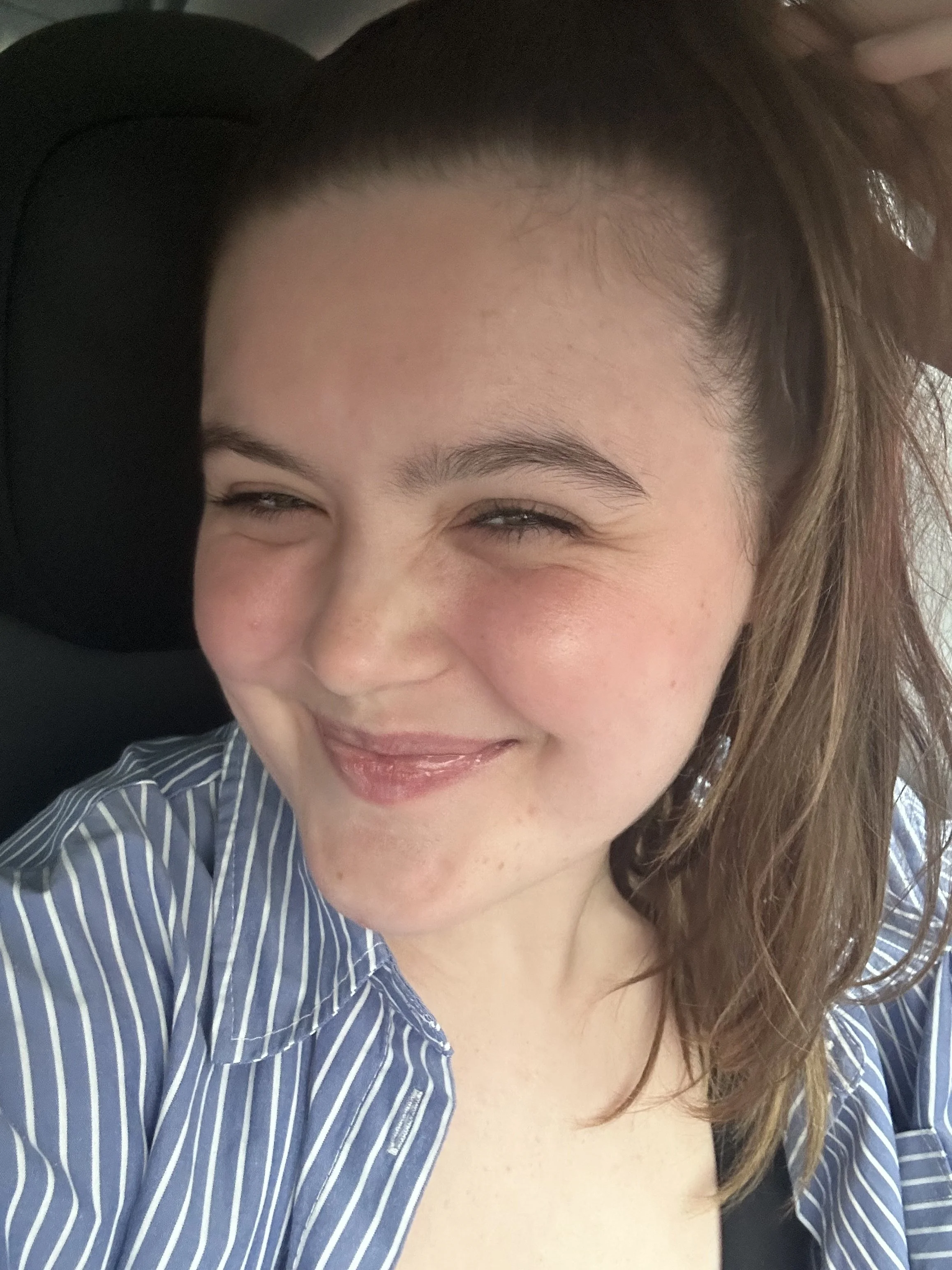 Abi Mack smiling with her eyes closed, wearing a blue and white striped shirt, and sitting in a car.