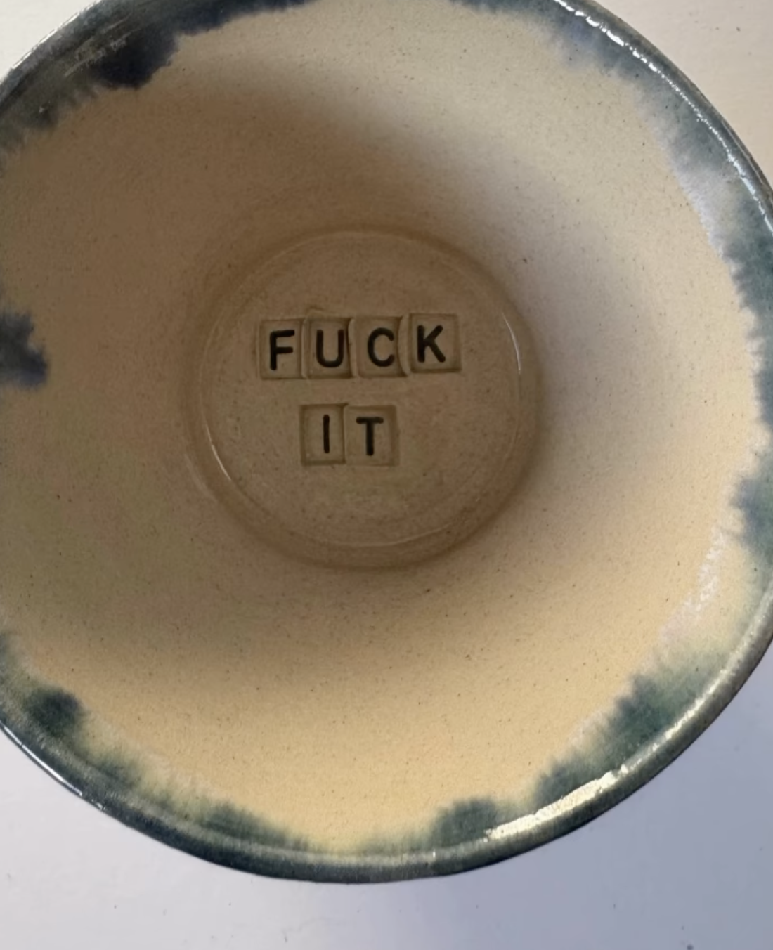 The bottom of a mug with Scrabble letter tiles spelling out 'FUCK IT' inside.