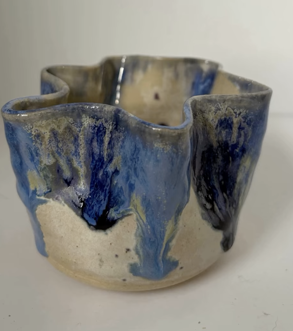 Ceramic bowl with an uneven, wavy rim, decorated with blue, black, and beige glazes, on a white surface