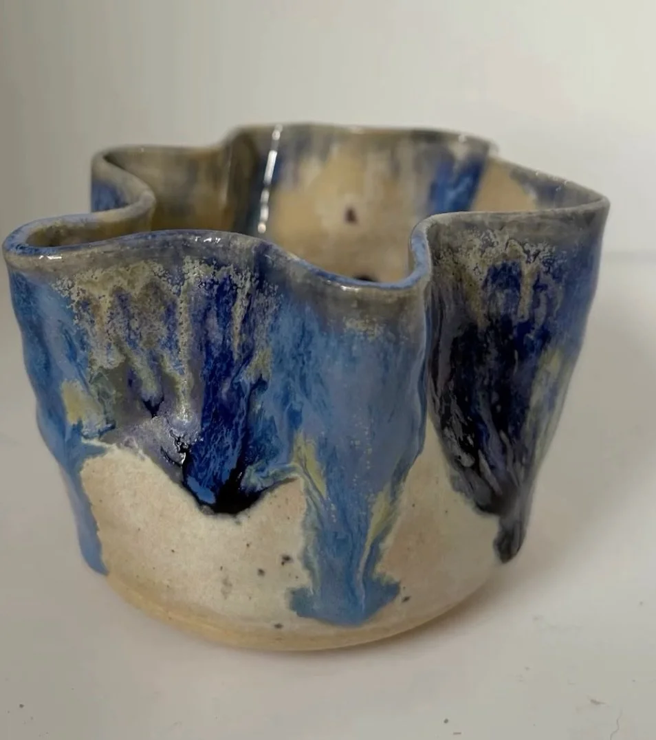 Ceramic bowl with a wavy edge, decorated with blue, black, and beige glaze patterns.