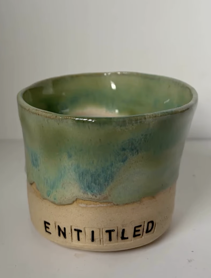 Ceramic cup with a green and beige glazed finish, with the word 'ENTITLED' spelled out in black letters on the beige base.