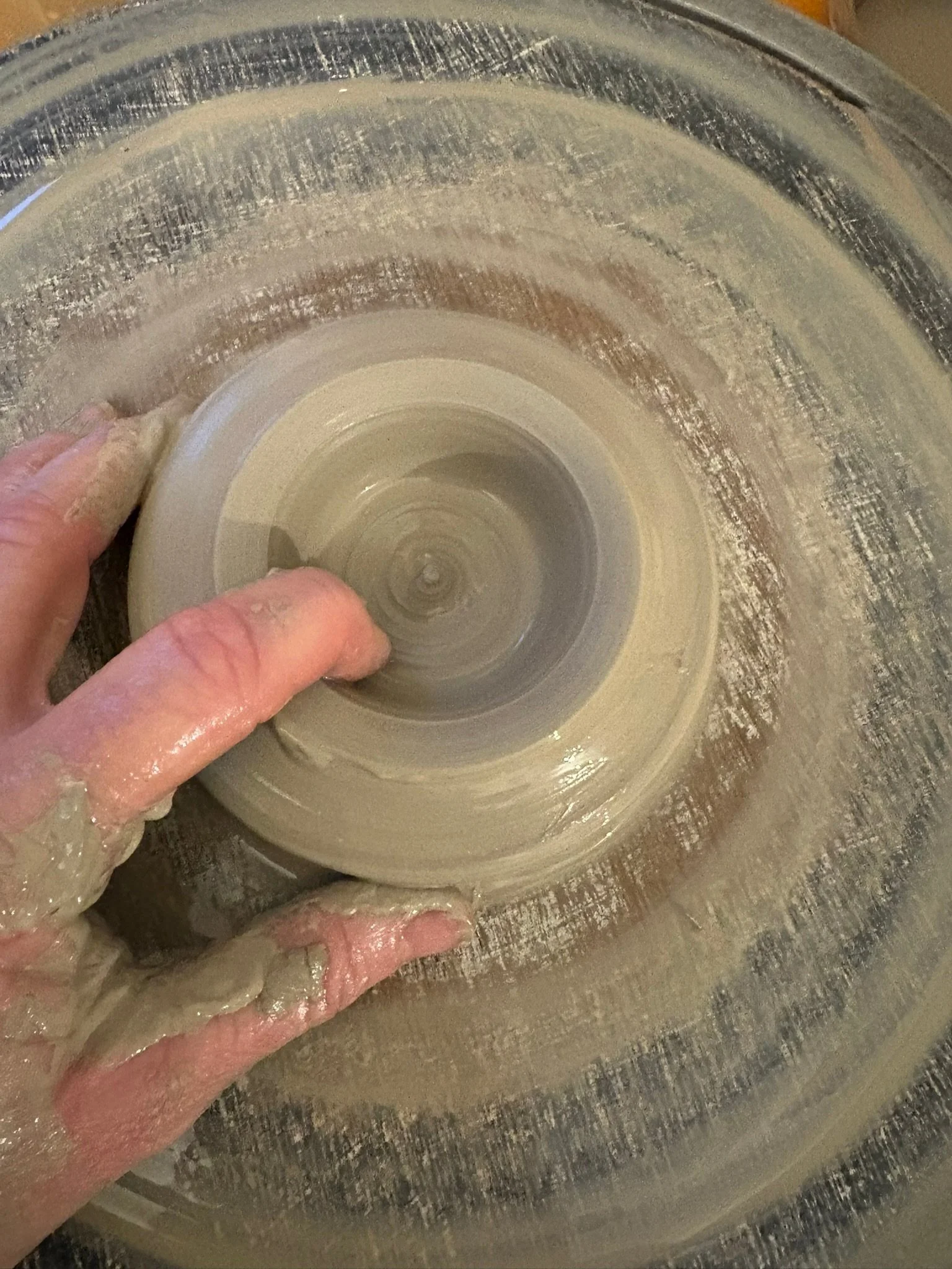 A person shaping a clay wheel on a pottery wheel, with their fingers pressing into the spinning clay.
