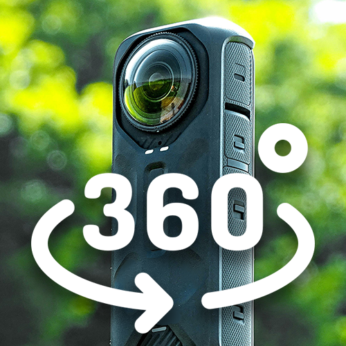 A 360-degree camera mounted on a black handheld stabilizer outdoors with green trees in the background.