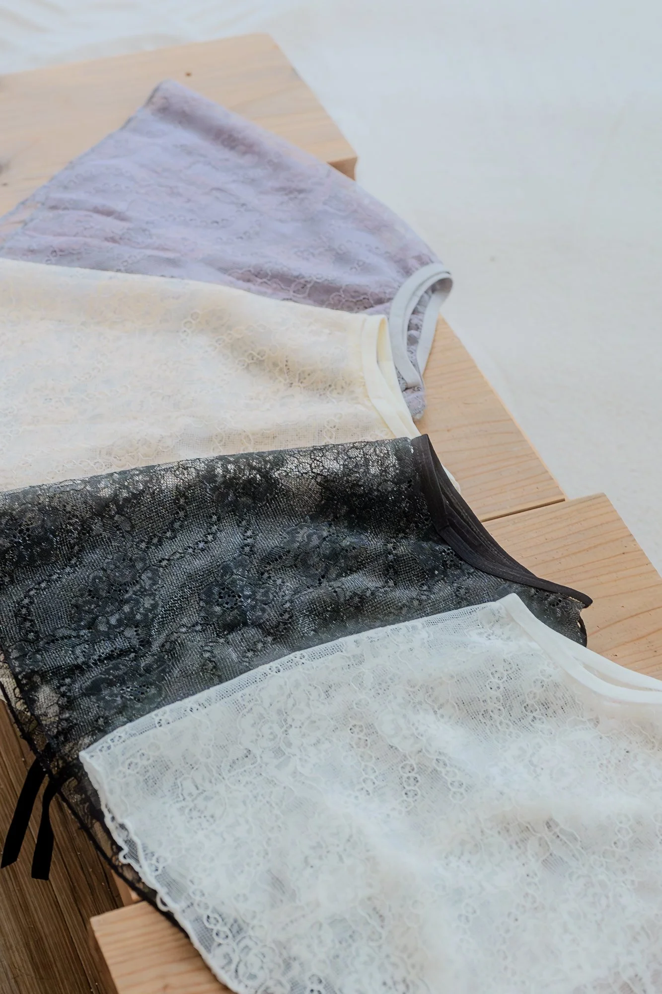 黒、白、クリーム色、灰色のレース柄の女性用下着が木製のテーブルに並んでいる画像