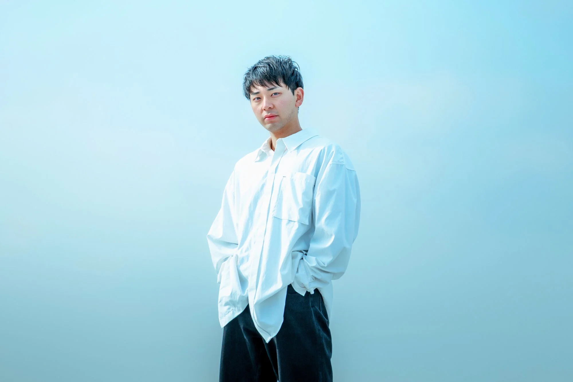 白いシャツを着た若い男性が青い背景の前に立っている
