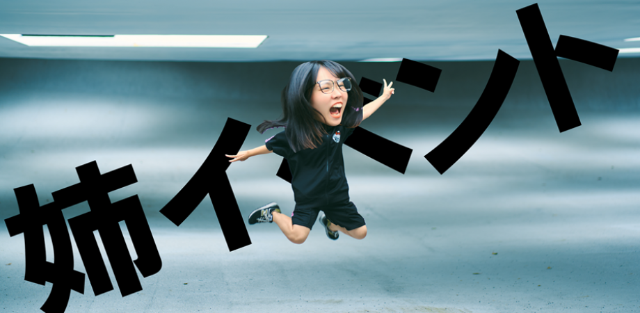 喜んでジャンプしている女性の写真、背景は緑色の壁と天井の照明、巨大な黒い文字で「姉イコー」と書かれている