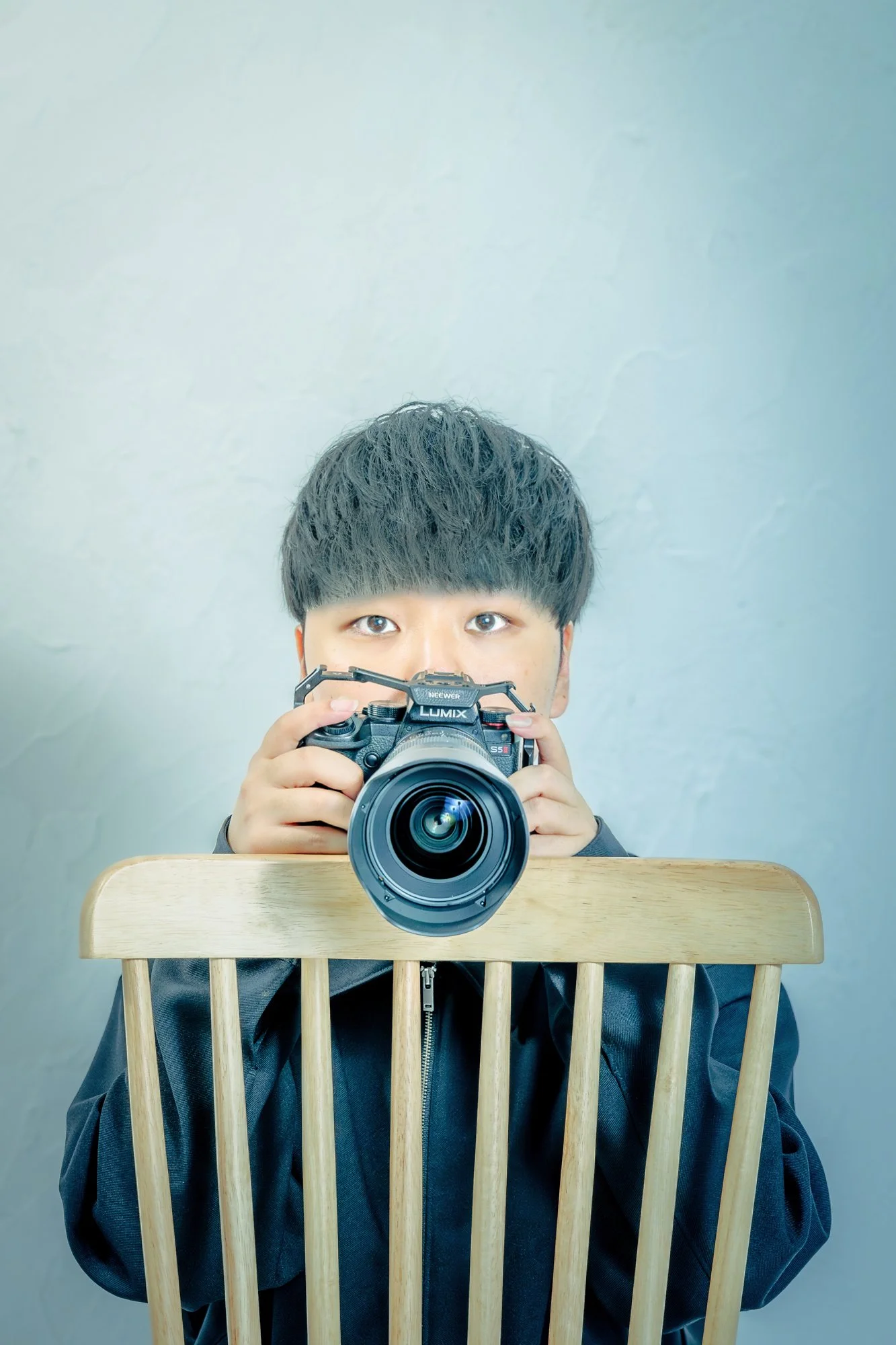 木の仕切りの前に座る少年がカメラで写真を撮っている