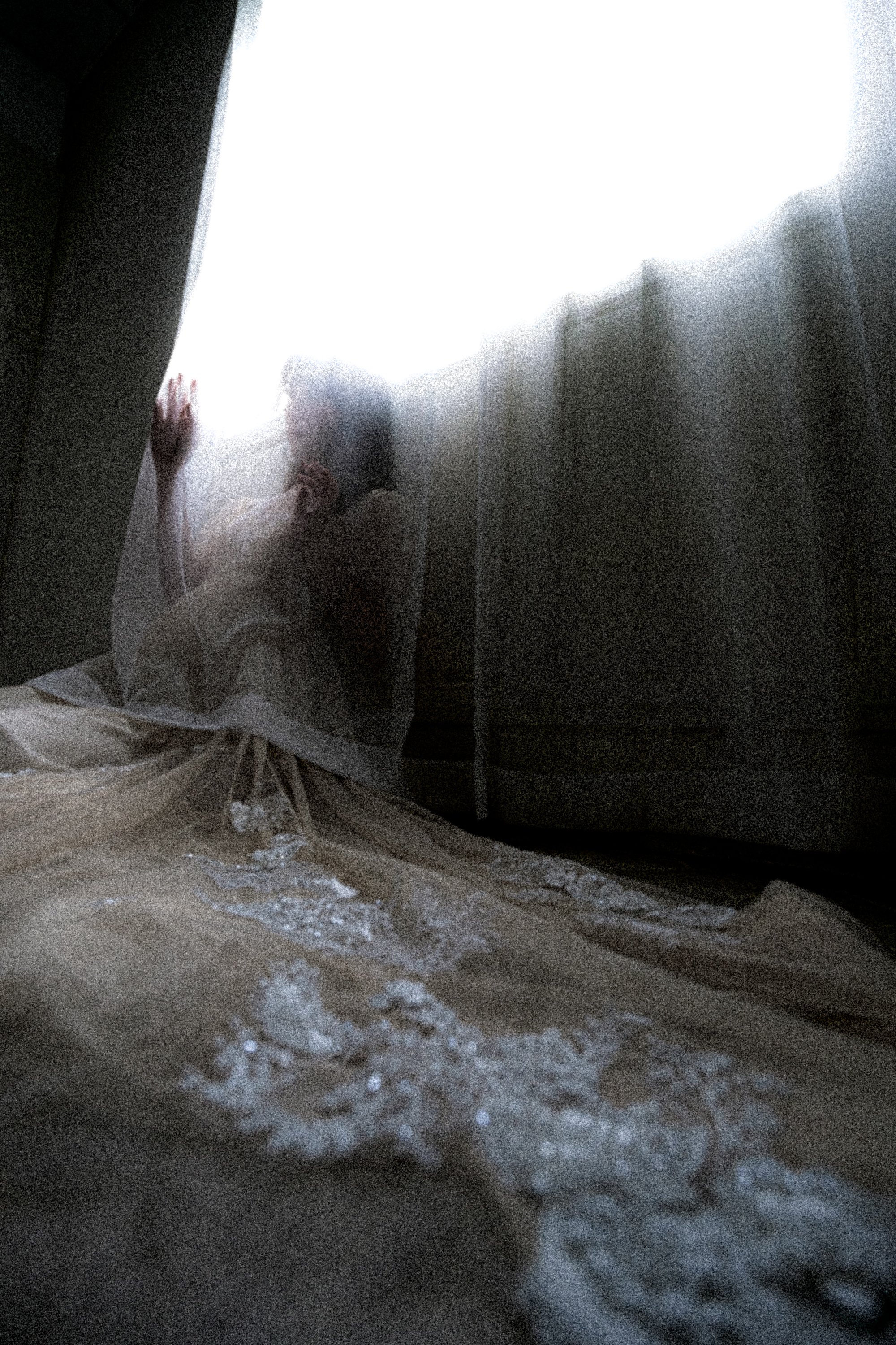 カーテンと光の間に人が腰をかがめているシルエット画像