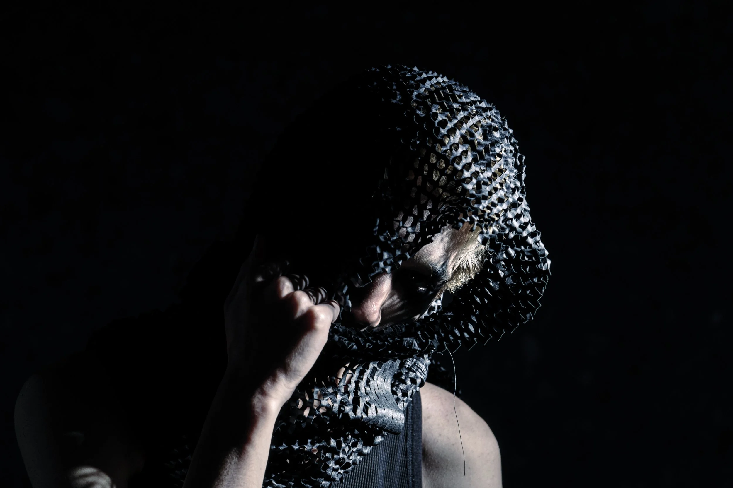 暗闇の中で、フード付きの衣服を身にまとった人物が顔を隠している