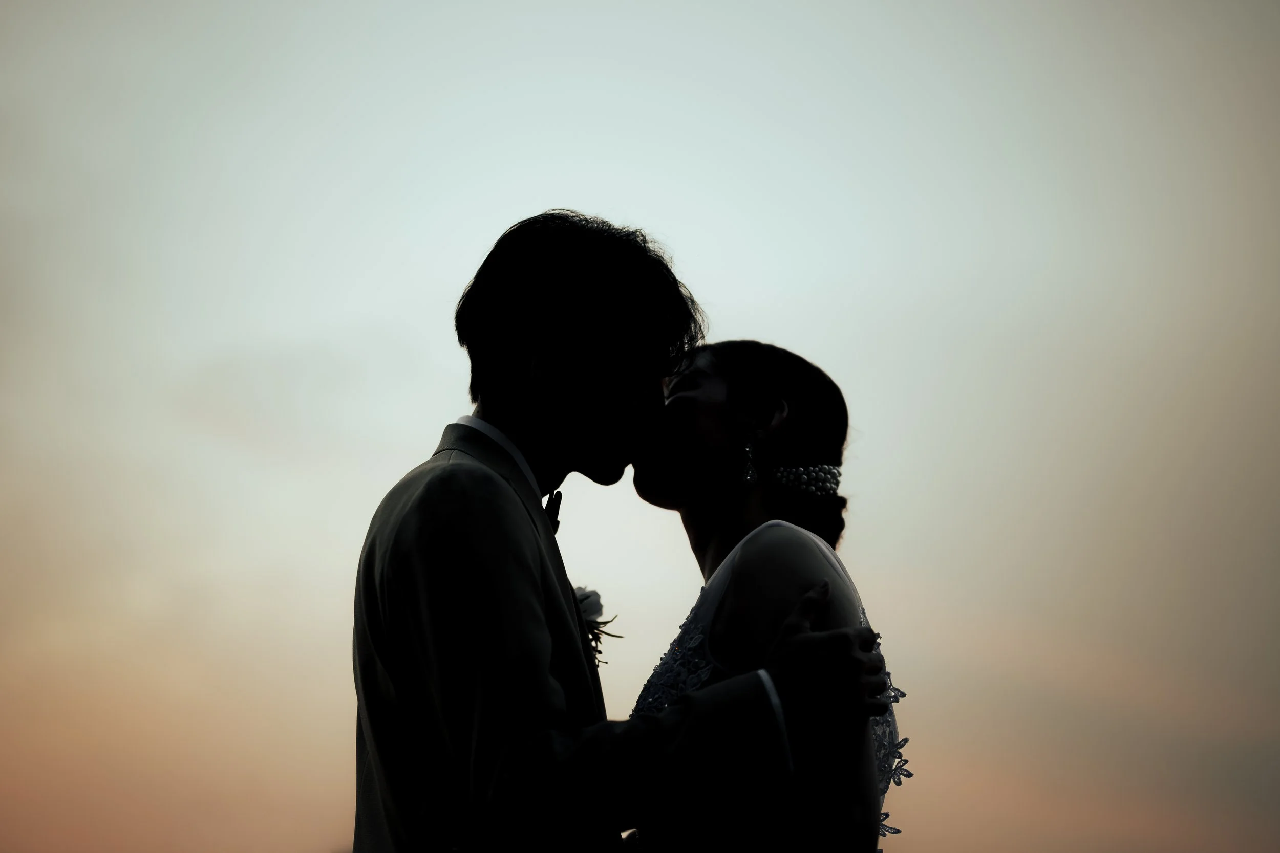 夕焼けの背景にシルエットの結婚したカップルがキスをしている