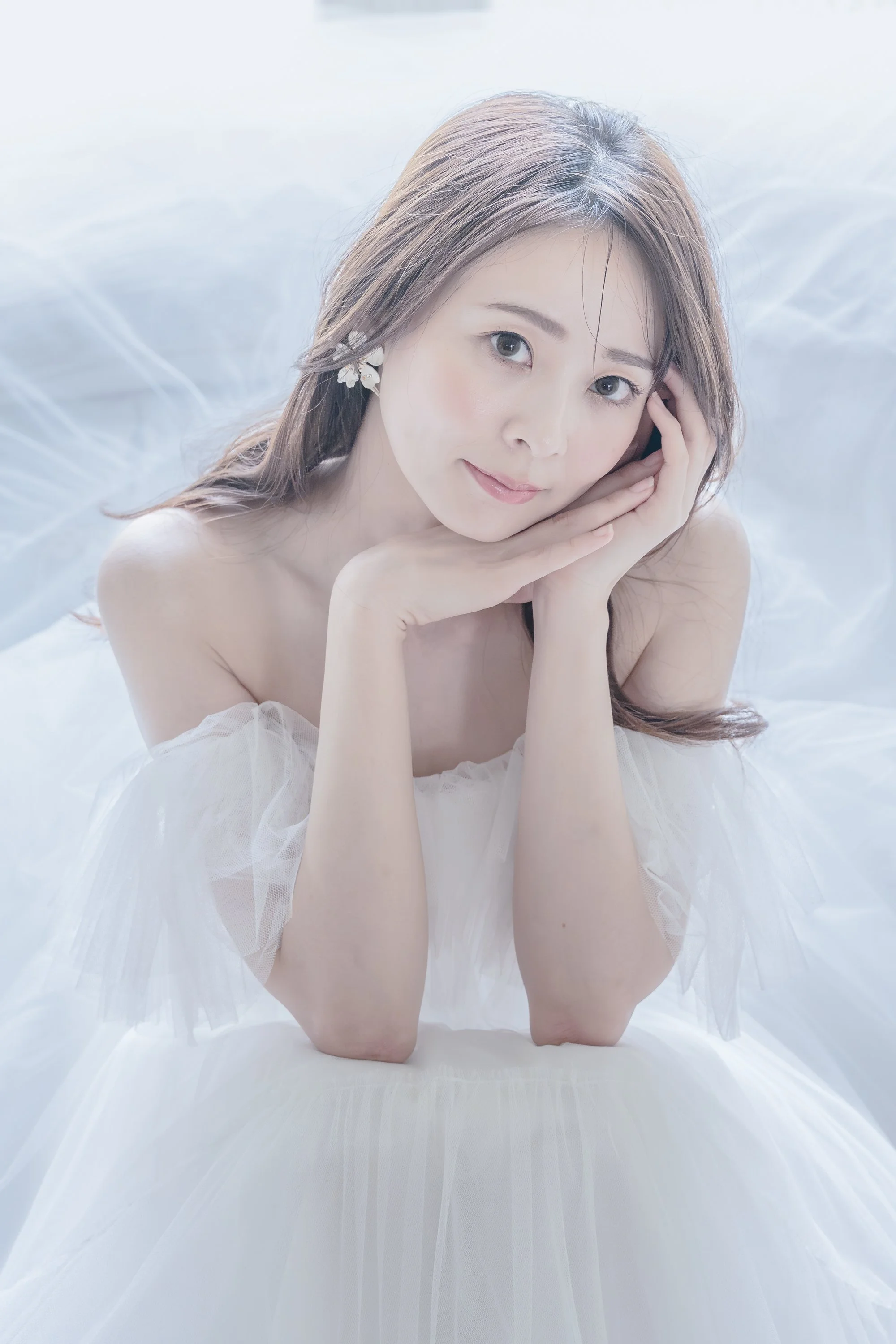 白いドレスを着た女性のポートレート写真で、柔らかい自然光の下で横になっている。