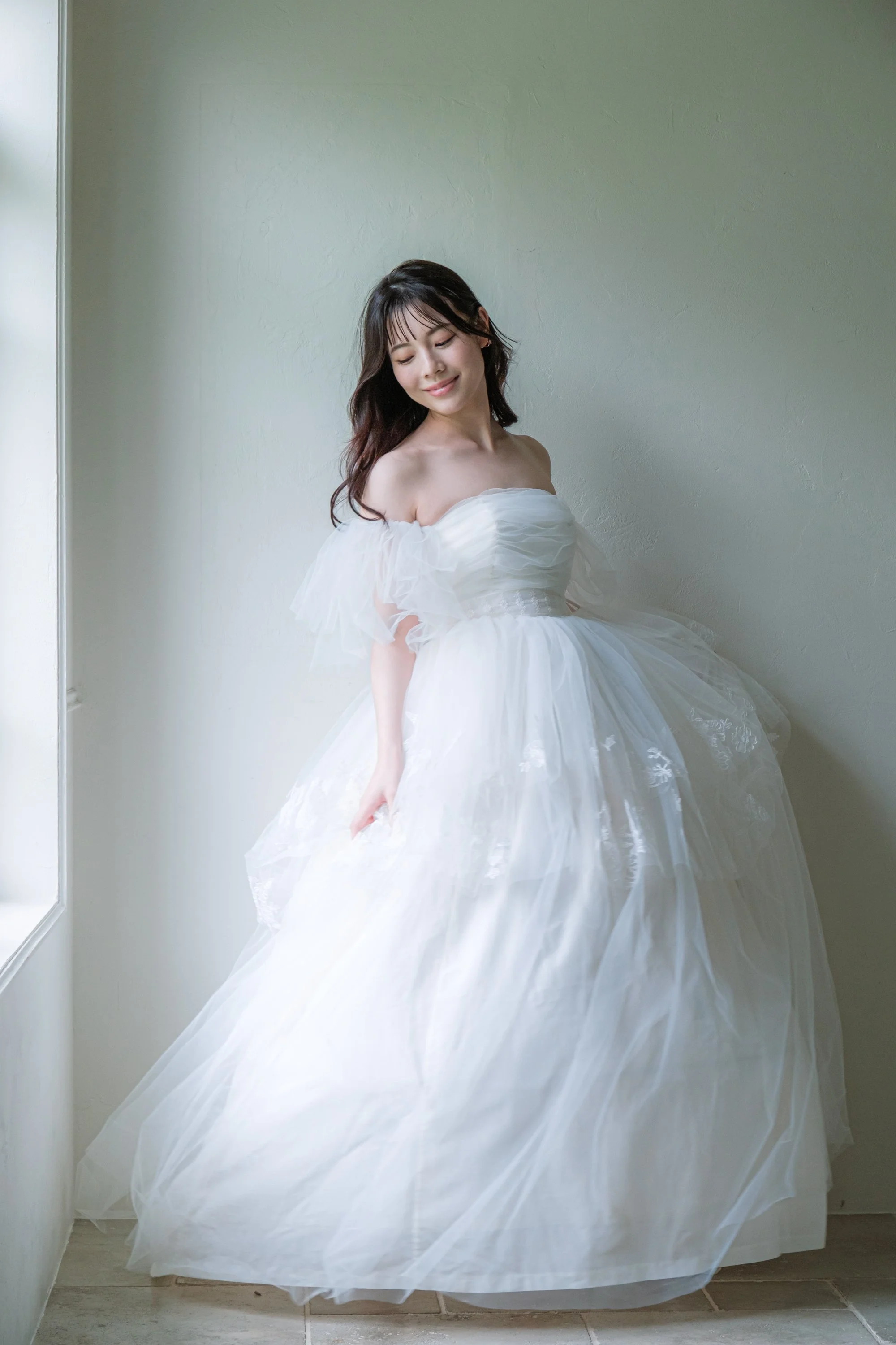 白いドレスを着た女性が窓辺に立っている