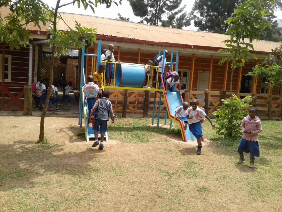 Children playing on a playground with slides and climbing equipment outside a school building.