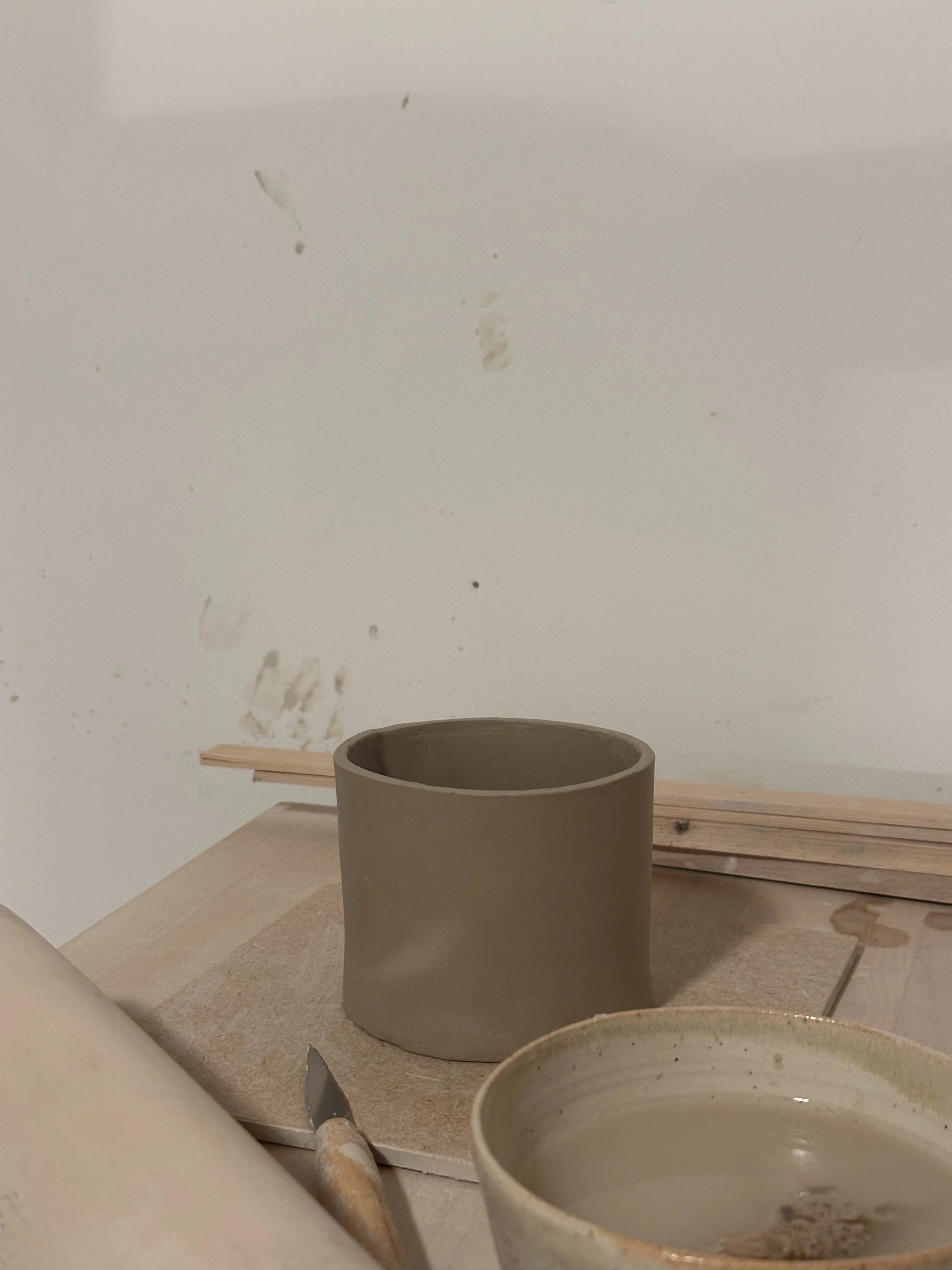 Clay to pot on a wooden workspace, with pottery tools and a bowl of water nearby.