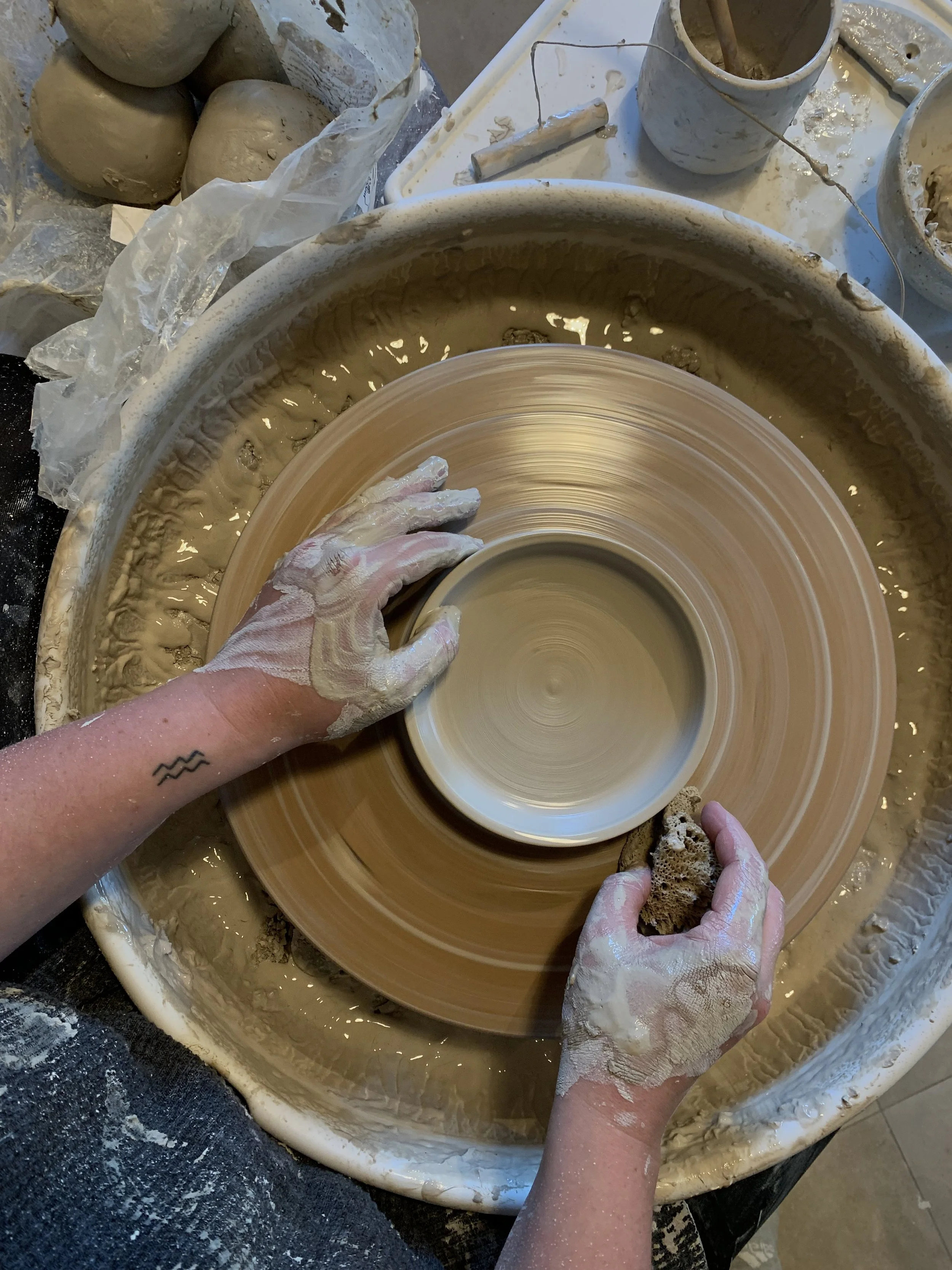 Personen, die an der Töpferscheibe Ton formen, mit Wasser bedeckt, in einem Töpferstudio.