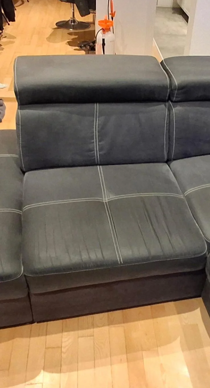 Tamna kožna sofa s bijelim šavovima u prostoru s opremom za čišćenje u pozadini
