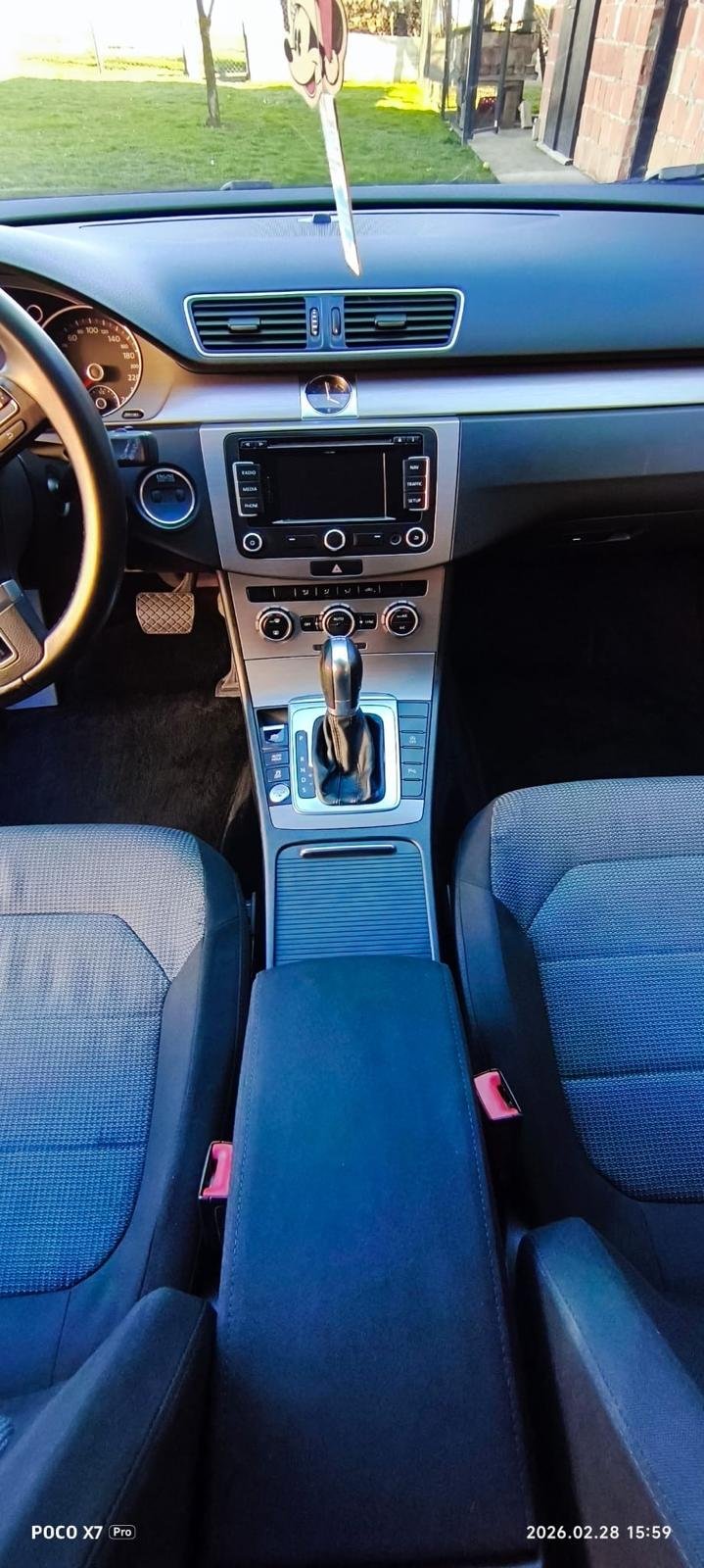 Interior view of a car cockpit showing the dashboard, steering wheel, center console with gear shift, air vents, and infotainment system, with two front seats.