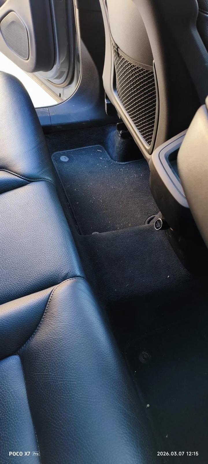 The back seat area of a car showing black leather seats, the car's floor, and the back of the front seats with storage pockets.
