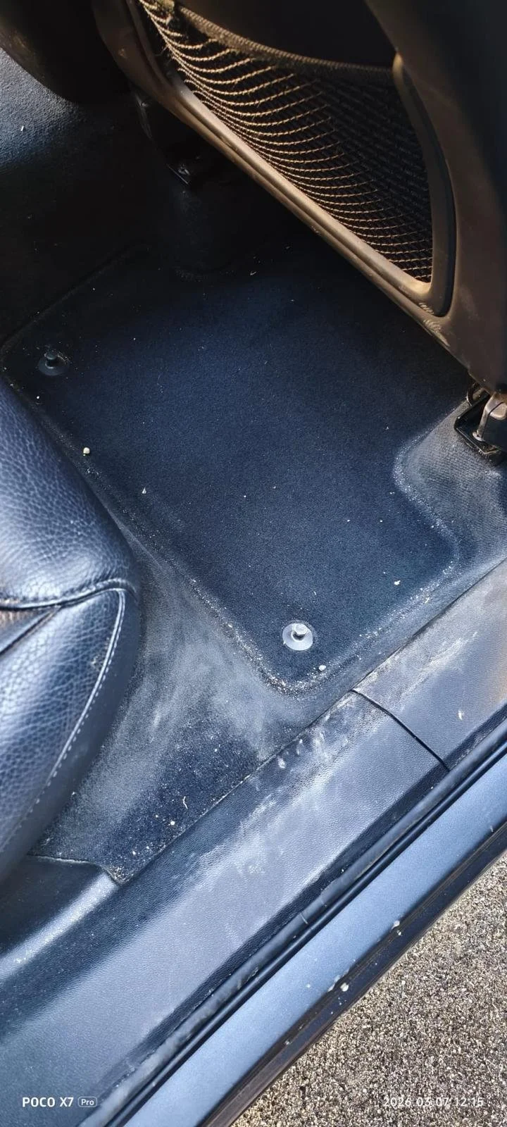 Car interior showing the lower part of the back seat and floor area with some dust and small debris.