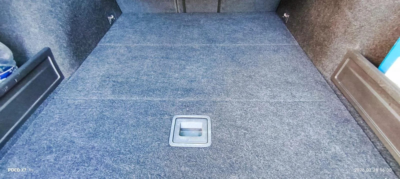 Inside an elevator with a gray floor and a square floor drain in the center. The walls are dark and brown, with some metal hardware visible.