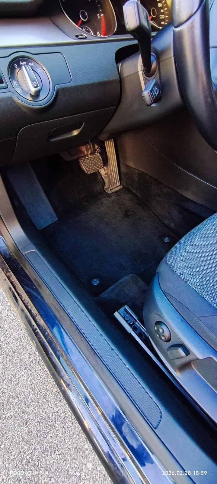 Interior of a car showing the driver's side, including the steering wheel, dashboard, foot pedals, and part of the seat.