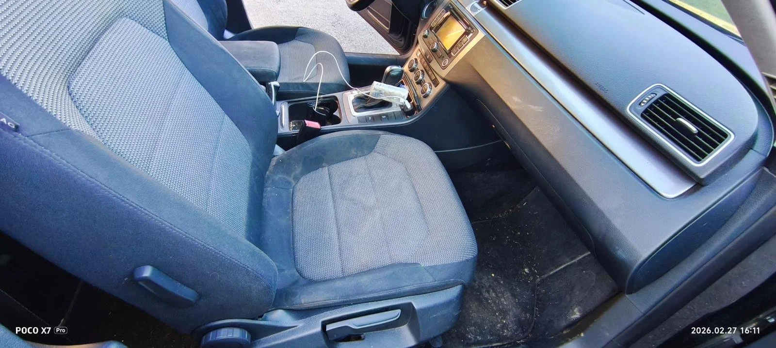 Interior of a car showing the front passenger seat, dashboard, and center console, with some dirt on the floor and items on the console.