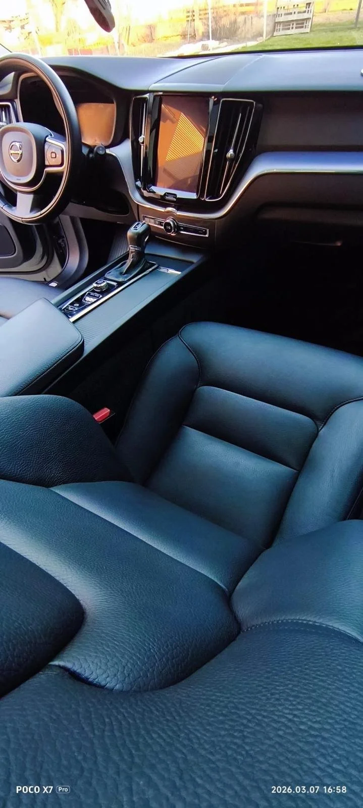 The interior of a modern Volvo car, featuring a leather seat, a central console with gear shift, and a large digital display on the dashboard.