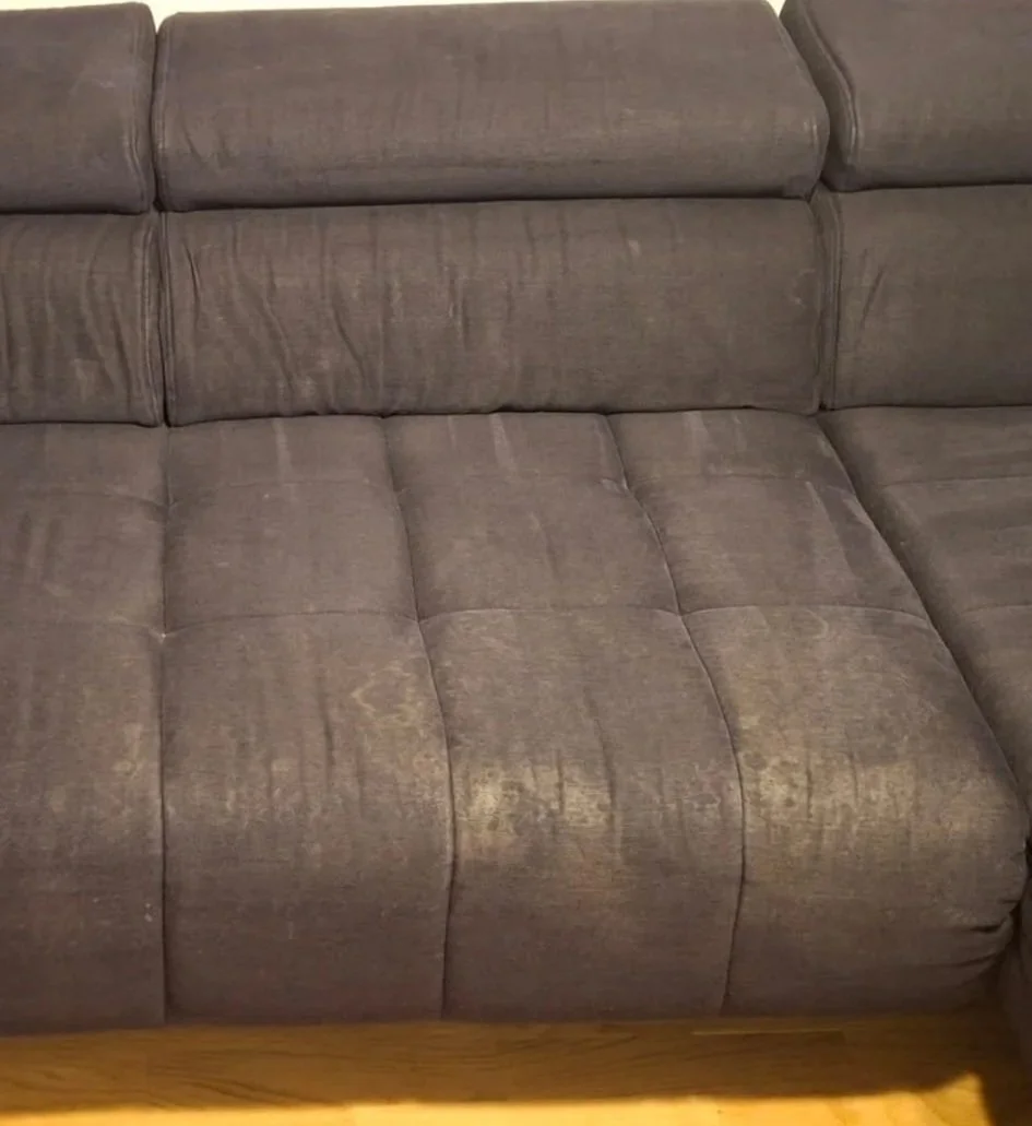 Smeđa sofa od tkanine s vidljivim trošenjem i mrljama na drvenom podu