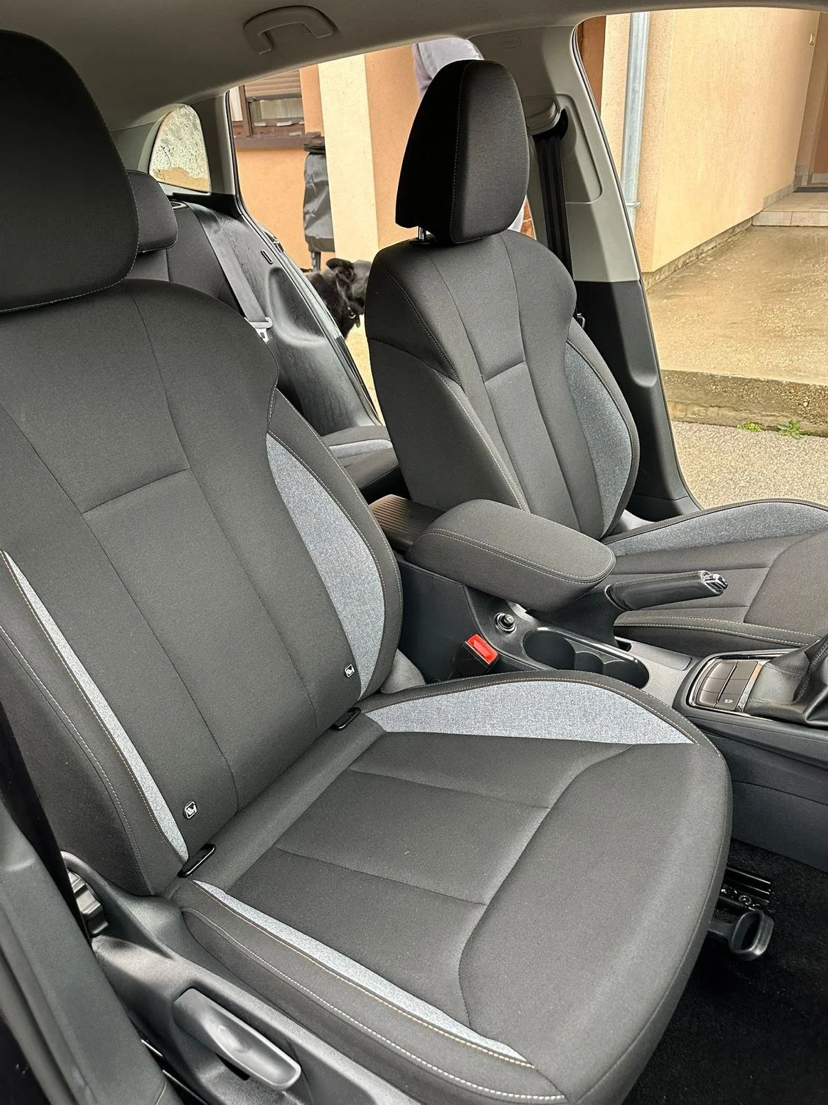 Prednji dio unutrašnjosti automobila sa sjedalima, središnjom konzolom i psom kraj prozora