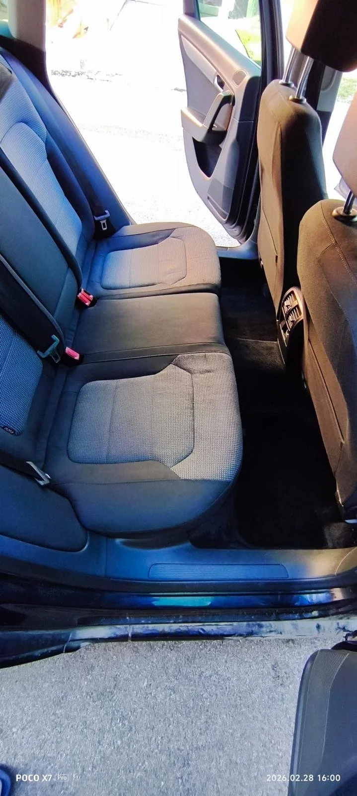 View of the back seat area of a car with a gray fabric interior, open rear passenger door, and visible front seats with beige and black headrests.