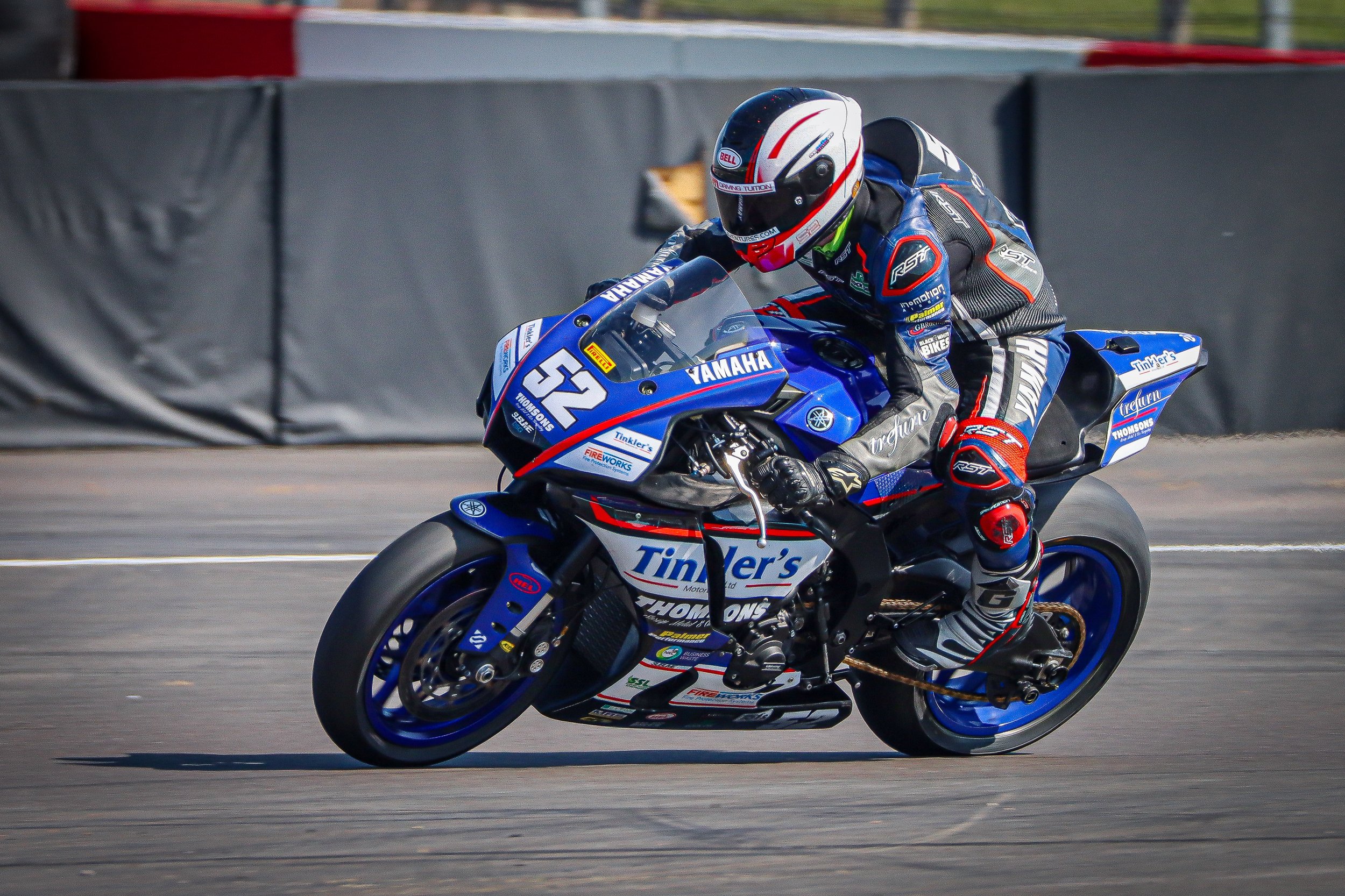 A motorcycle racer in a black, blue, and red suit riding a blue Yamaha motorcycle with the number 52 on a racetrack.