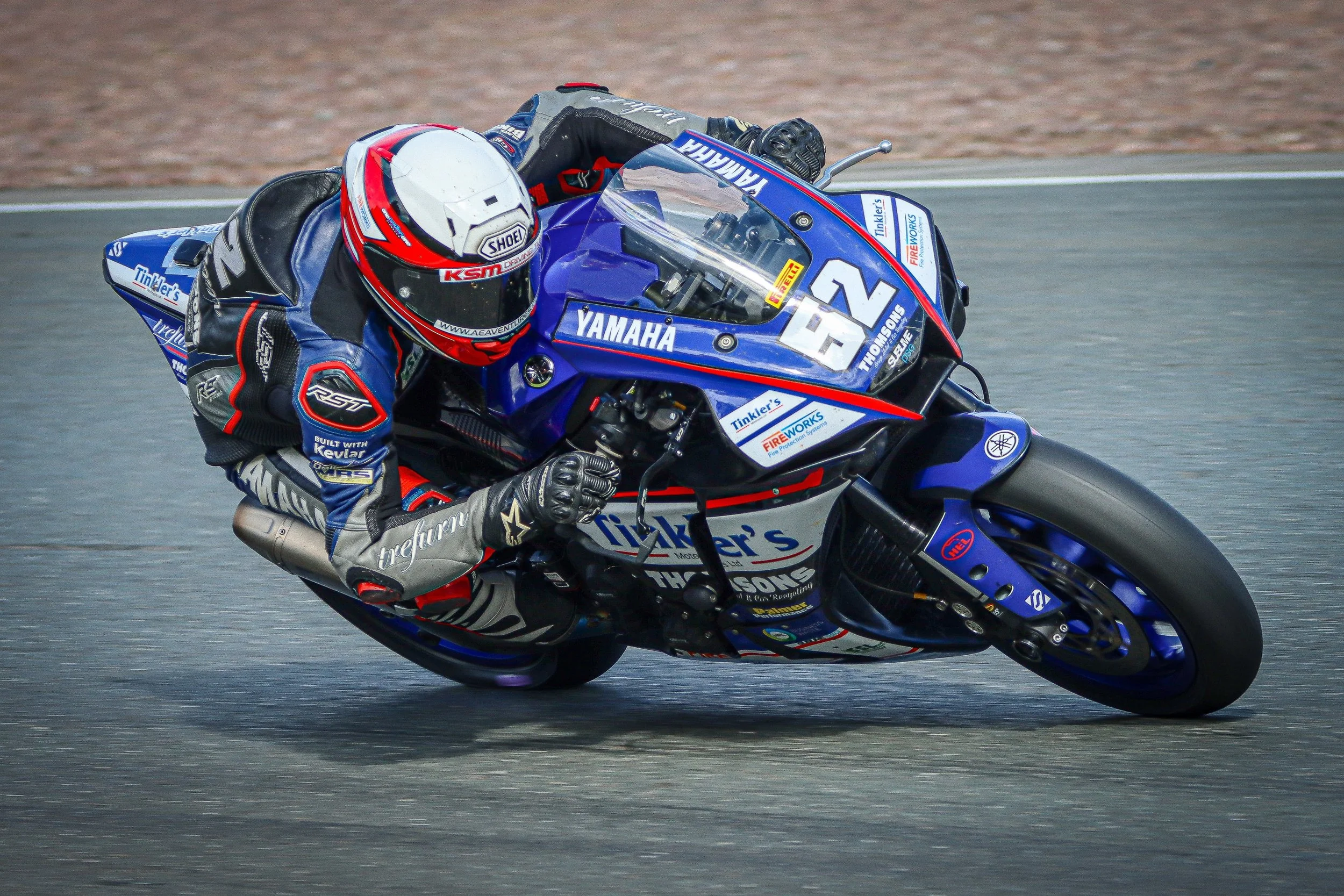 A motorcycle racer in racing gear leaning into a turn on a race track, riding a blue Yamaha motorcycle.