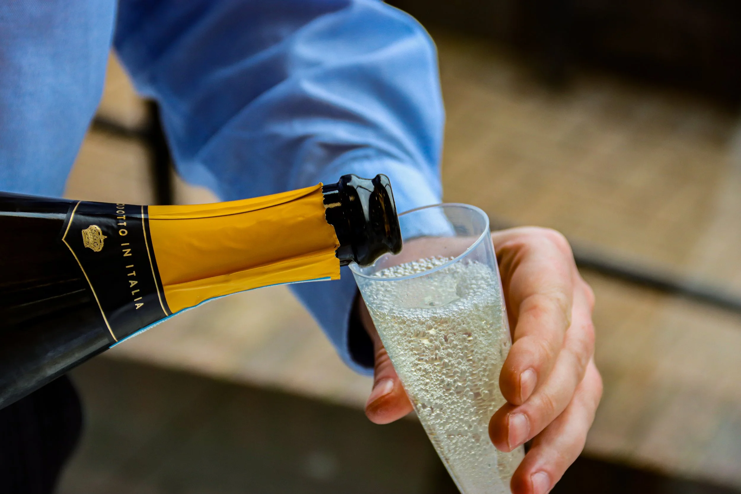 Person pouring champagne into a tall glass, holding it with one hand, with the bottle labeled 'Product of Italy'.