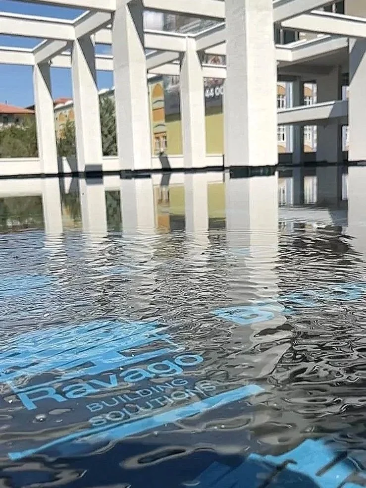 A modern building with white structural elements, large glass windows, and reflections in water in the foreground with the words "Ravas Building Solutions" written on it.