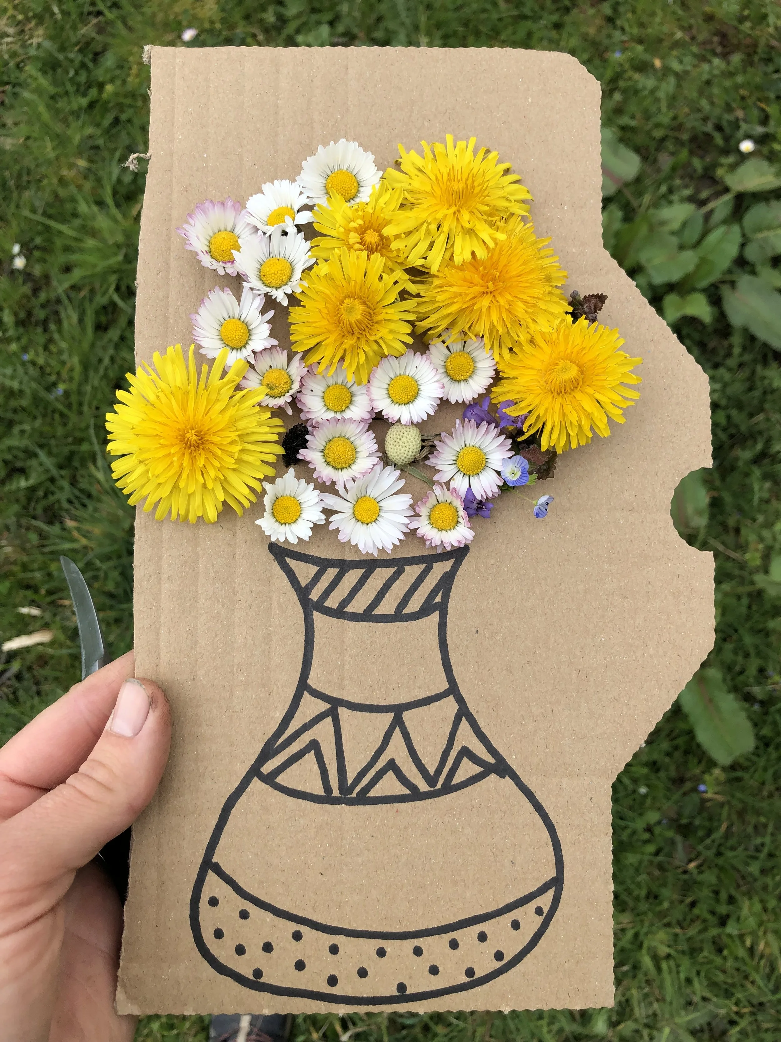Un bouquet de fleurs colorées, principalement de marguerites et de dandelions, placé sur une feuille de papier brune avec un dessin noir d'un vase.