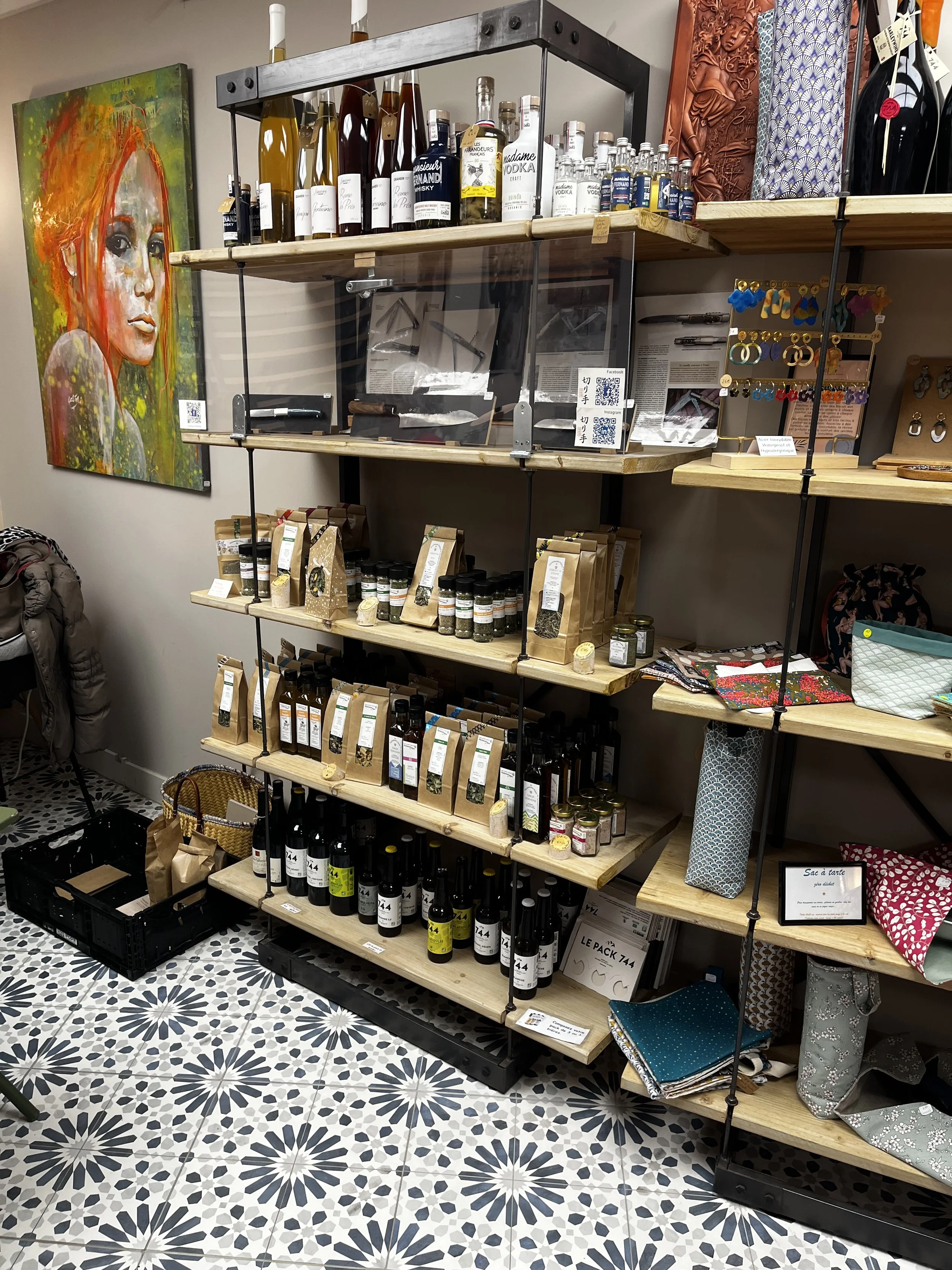 Étagères en bois avec des bouteilles d'alcool, bocaux, sacs en tissu et accessoires de mode dans une boutique, mur avec une peinture d'une femme aux cheveux rouges.