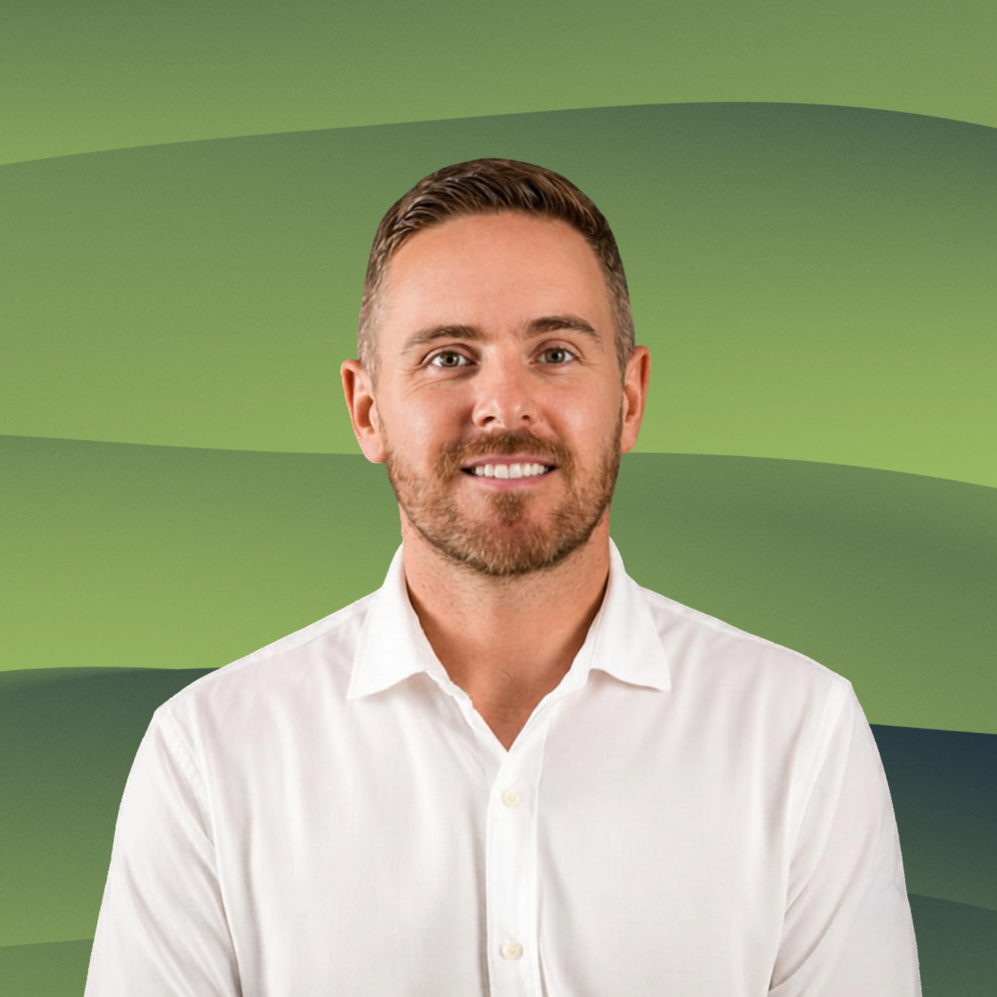 A man with short light brown hair and a beard, wearing a white dress shirt, smiling, standing in front of a wooden panel background.