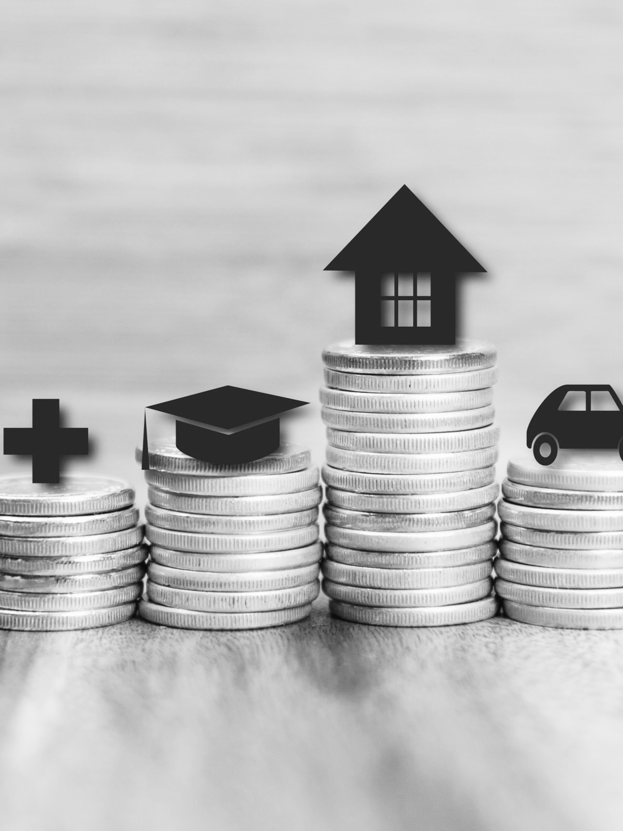 Stacks of coins with icons of a cross, graduation cap, house, and car placed on top.
