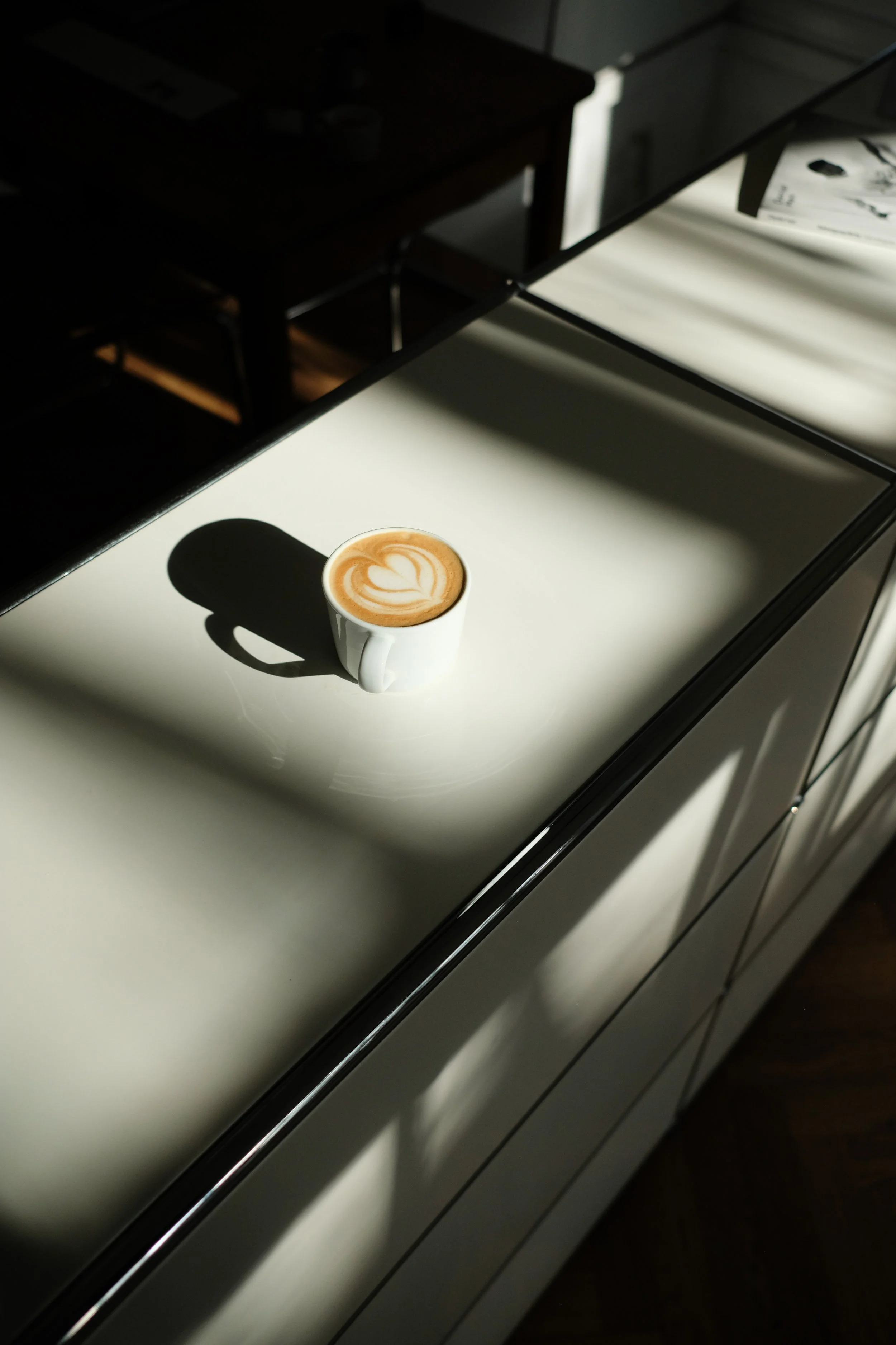 Eine schön zubereitete Latte steht in der Sonne auf der Reihe weißer Schränke im vorderen Raum der Physiotherapiepraxis.